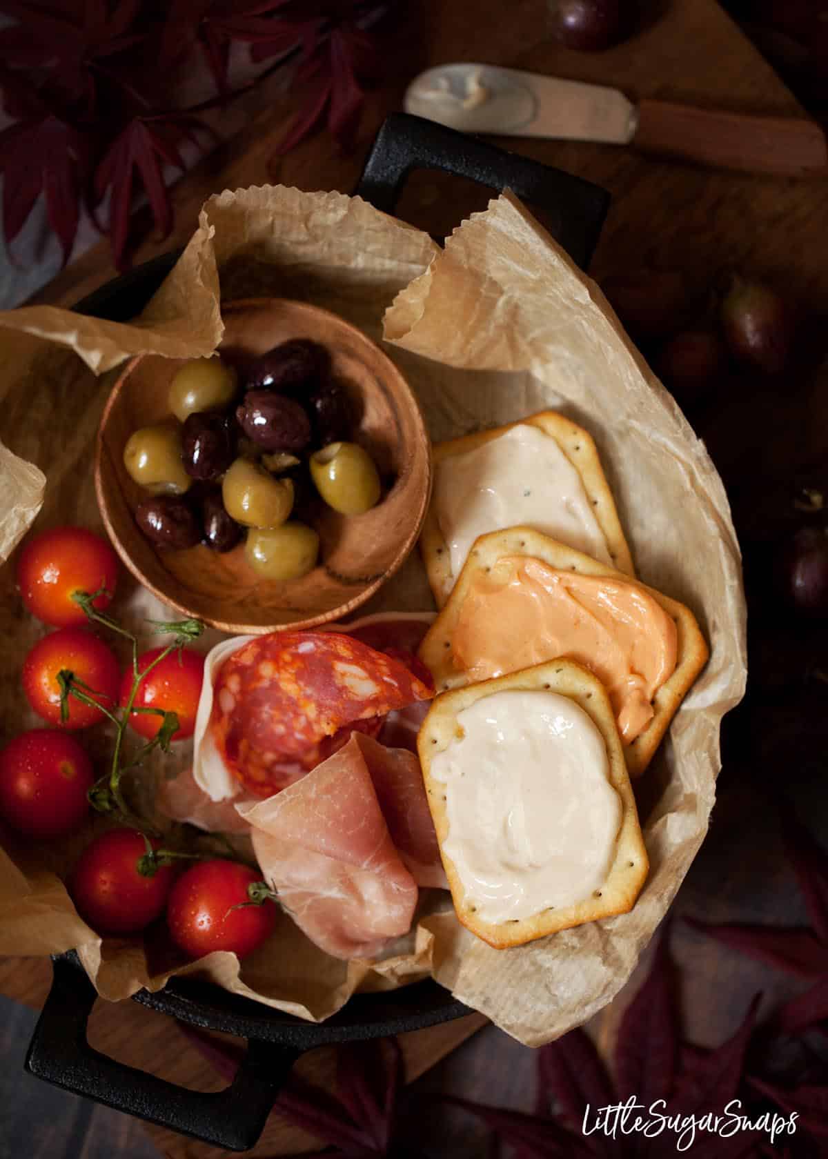 Crackers with cheese spread, olives, cured meats and cherry tomatoes on the vine.