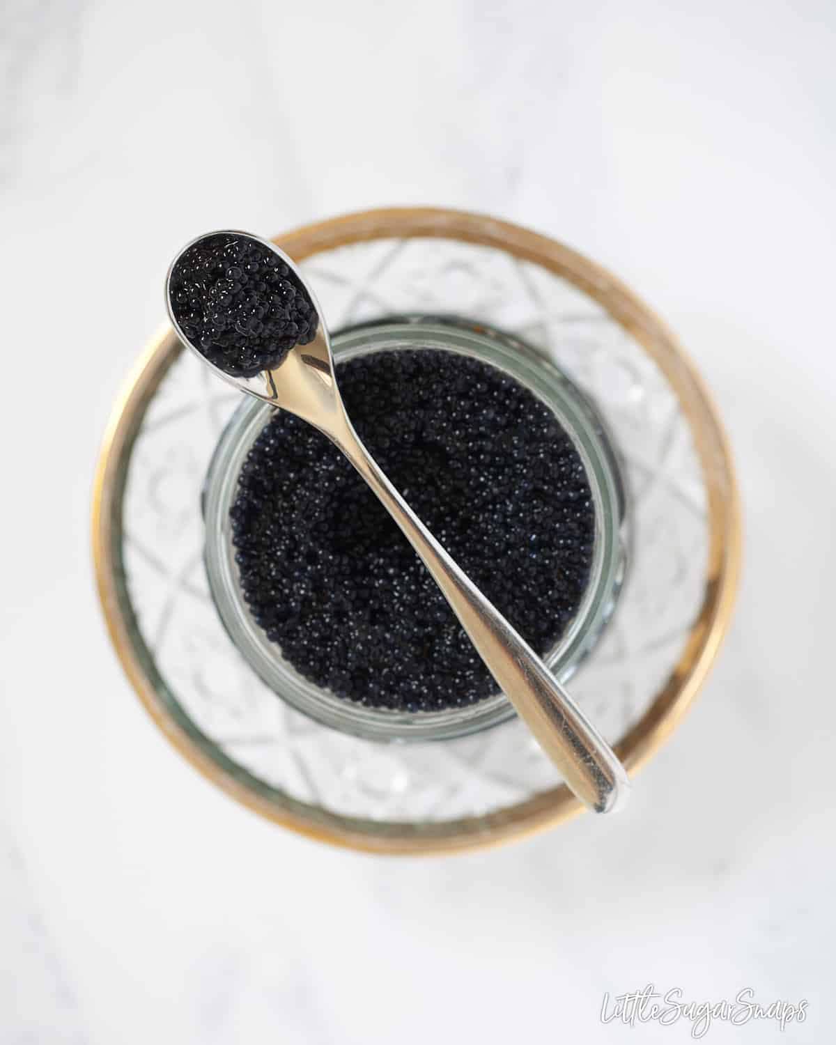 An open glass jar of caviar on a pretty plate. 