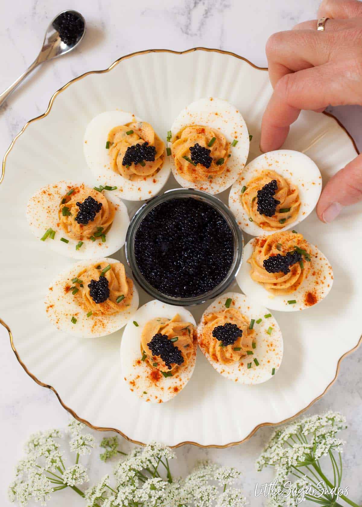 Person taking a devilled egg with caviar from a plate.