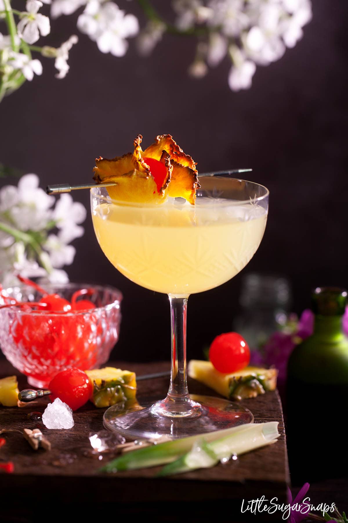 A gin and pineapple cocktail garnished with dried pineapple and maraschino cherry. 