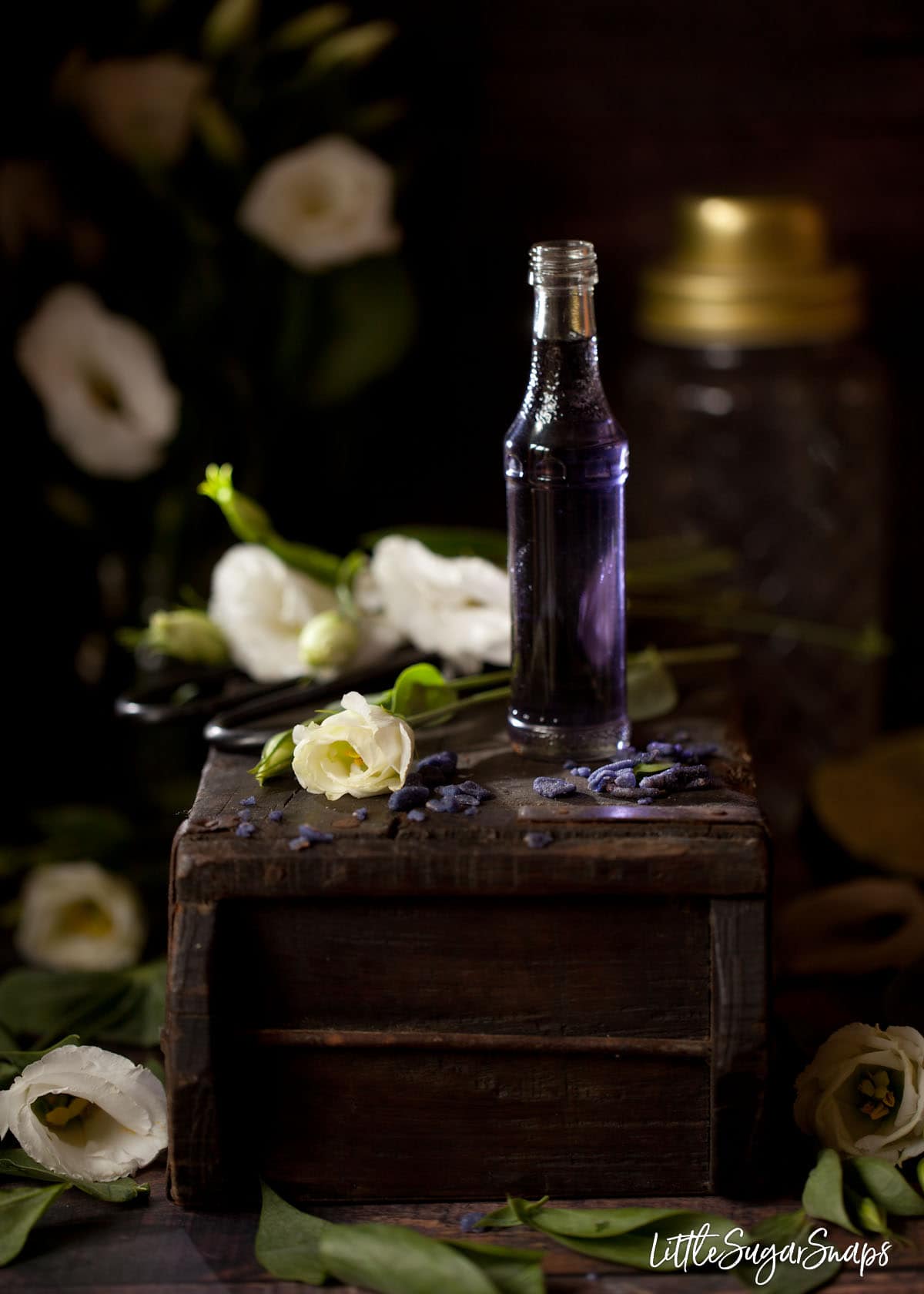 A small bottle of violet flavoured syrup on a wooden block with candied violet pieces