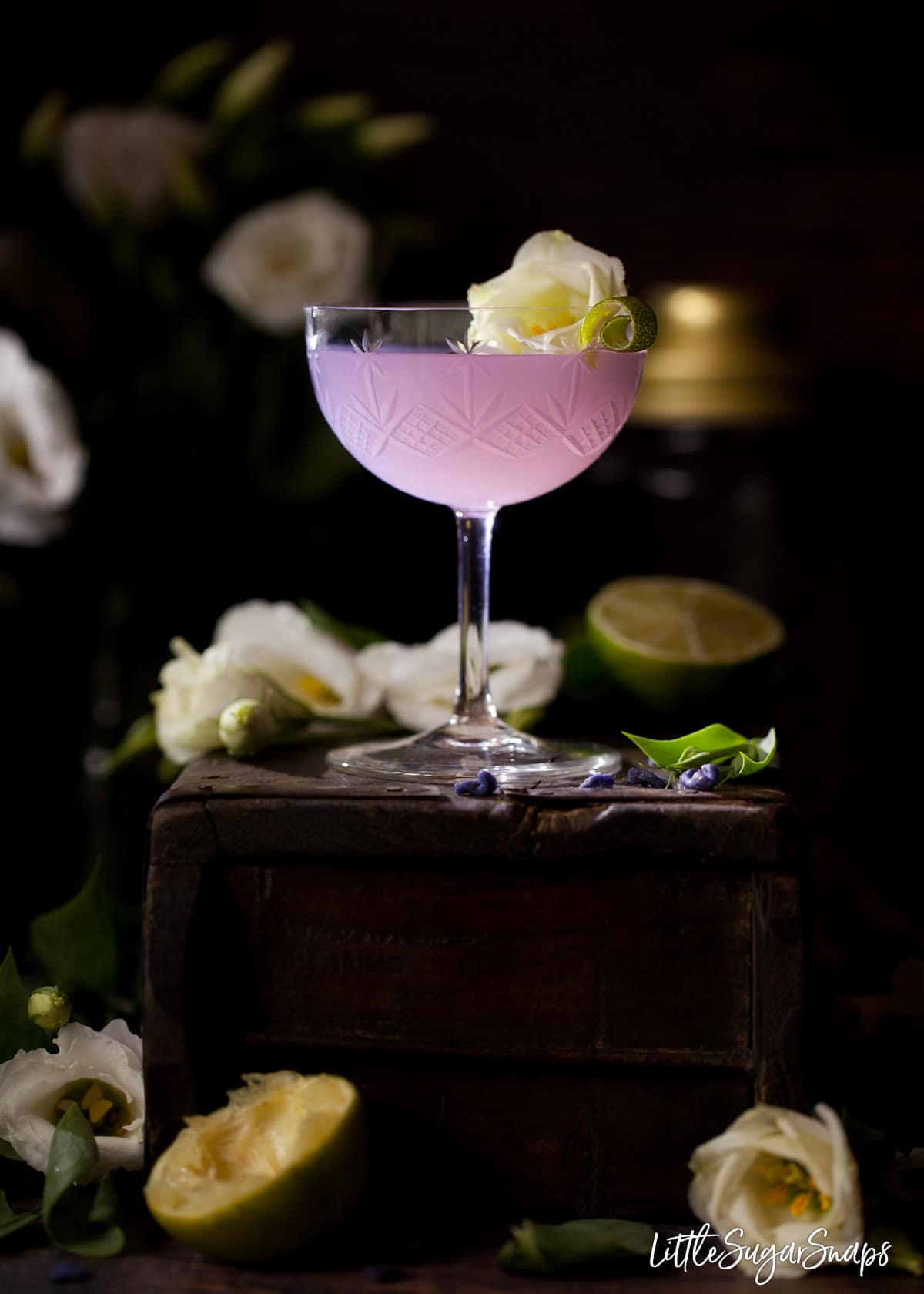 A violet cocktail garnished with lime and a white flower