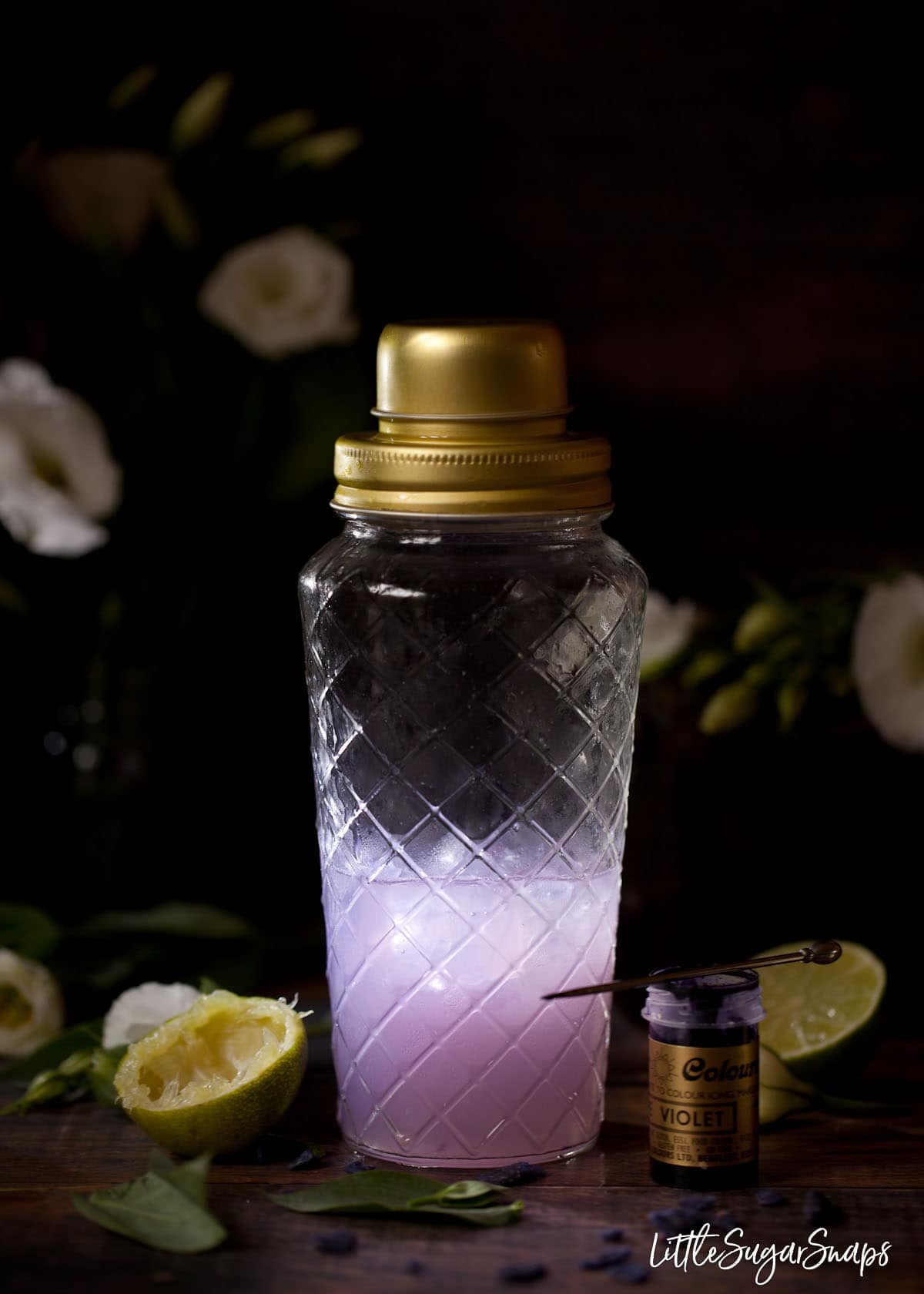 A purple violet cocktail in a shaker with food gel next to it