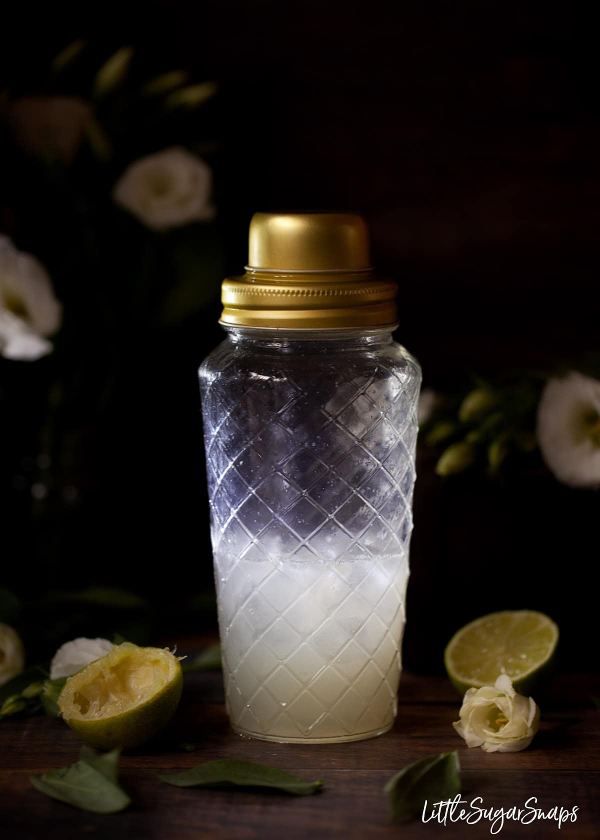 Cocktail ingredients in a glass shaker with lime halves next to it