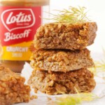 Three squares of Biscoff flavoured flapjack with a jar of Biscoff spread behind them.