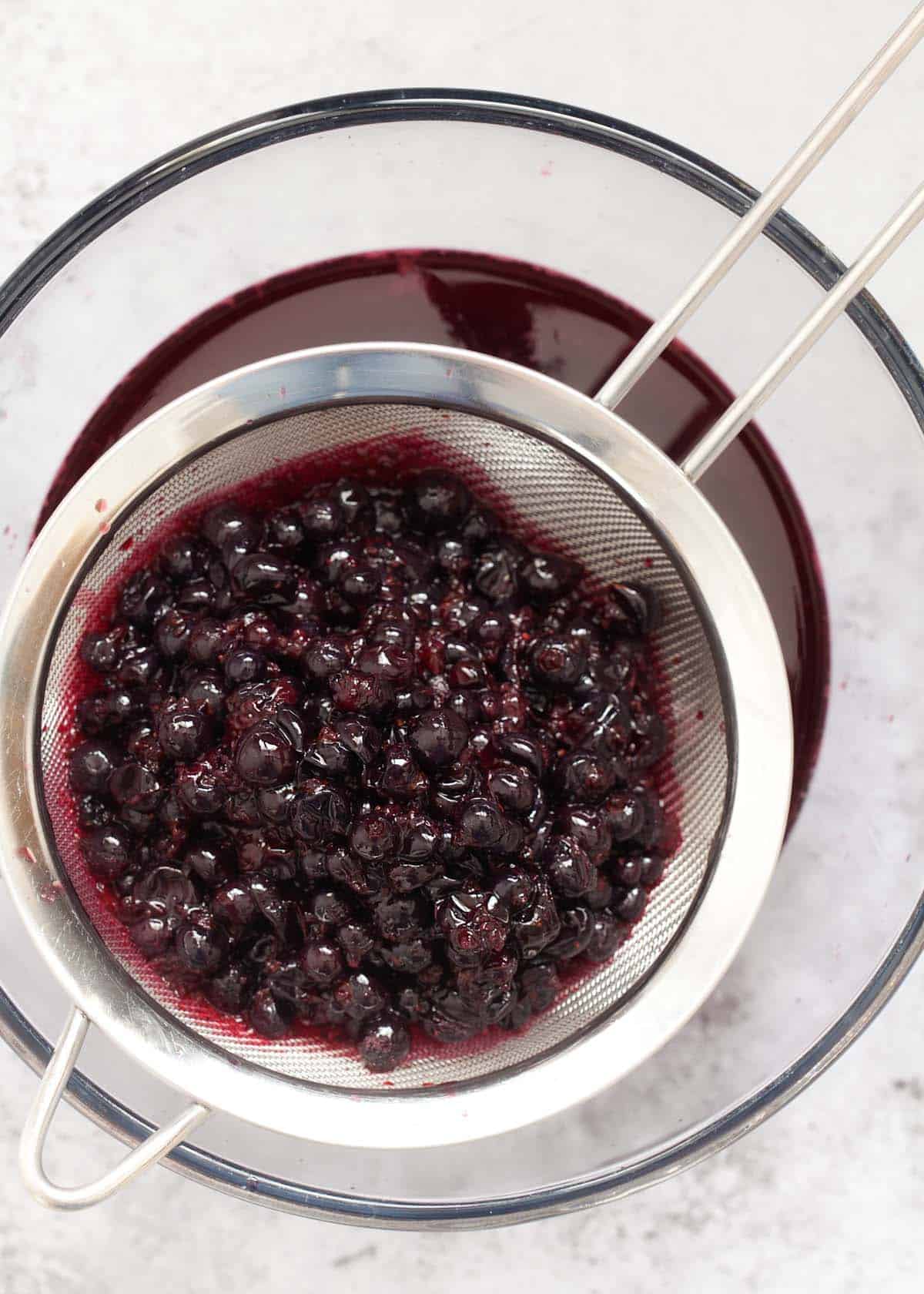 Straining cooked blackcurrants through a sieve to remove pulp