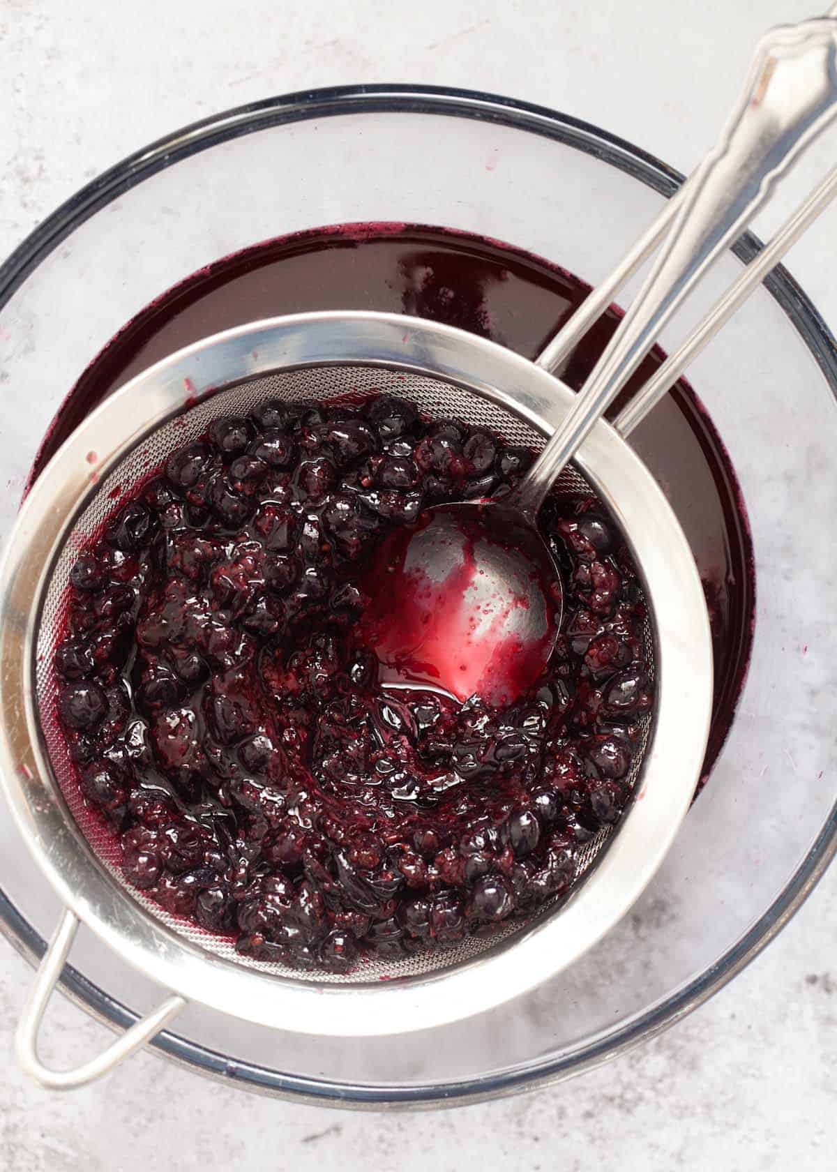 Straining cooked blackcurrants through a sieve to remove pulp