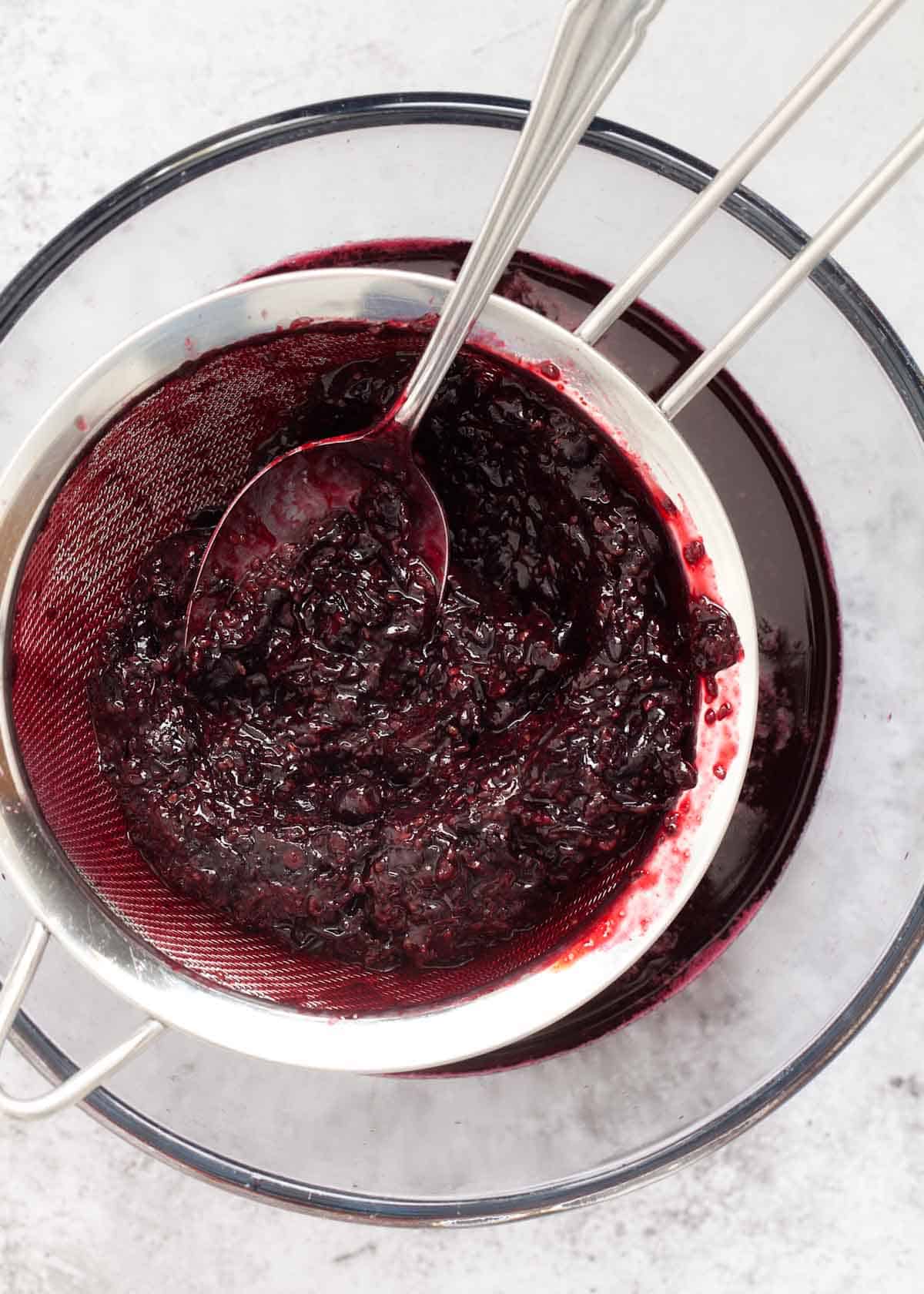 Straining cooked blackcurrants through a sieve to remove pulp