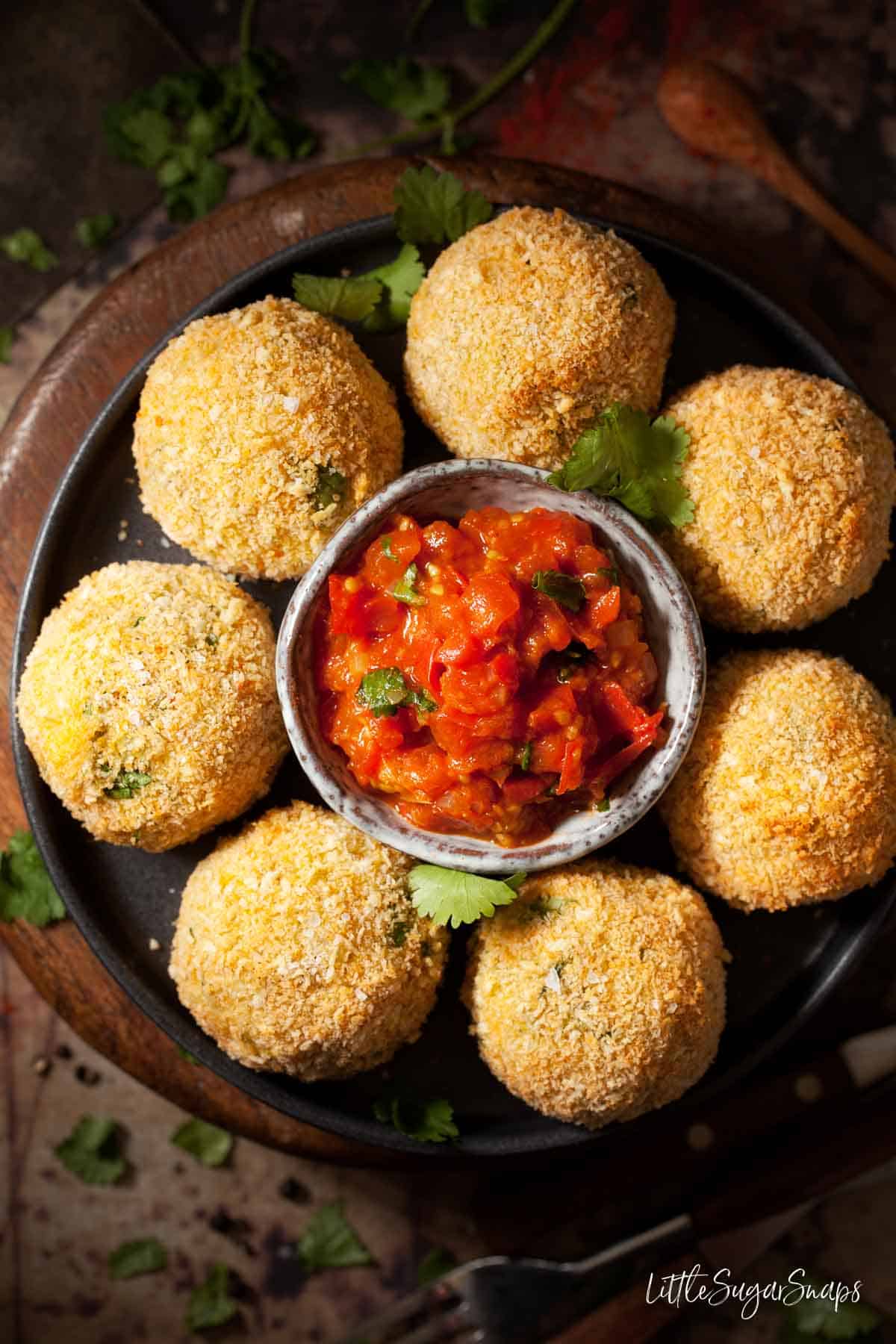 Fish cakes with haddock on a plate with a bowl of spiced tomato sauce.