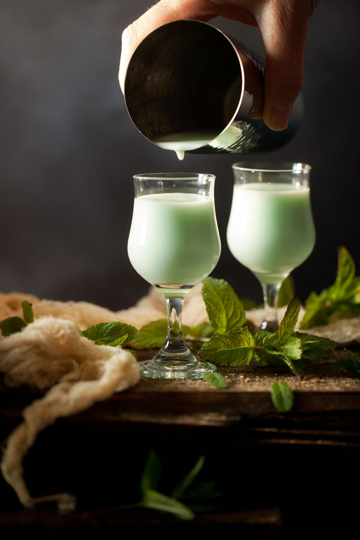 Pouring a pastel green creamy mint cocktail into vintage glasses from a cocktail shaker