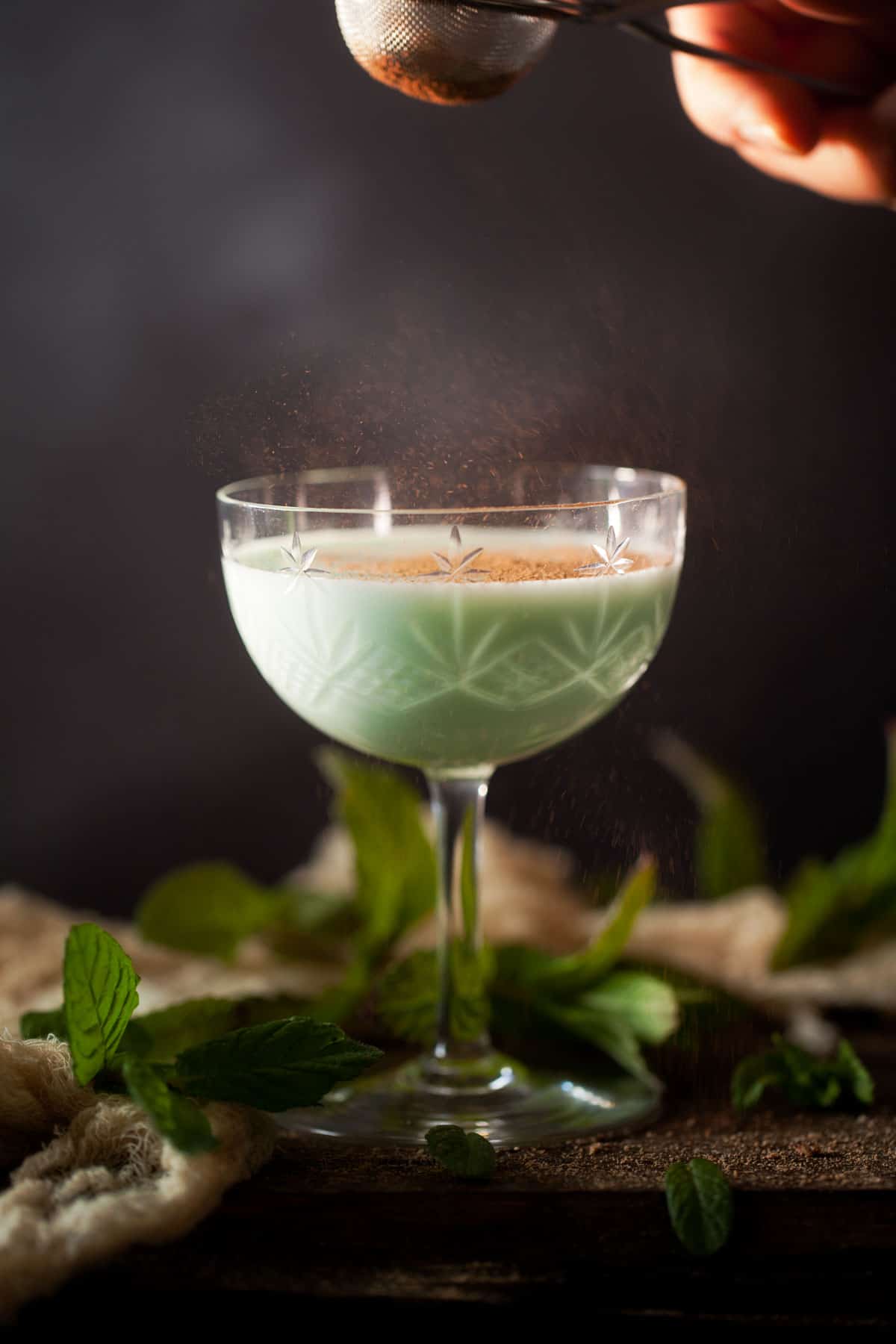 Cocoa powder being dusted onto a mint gin alexander cocktail 