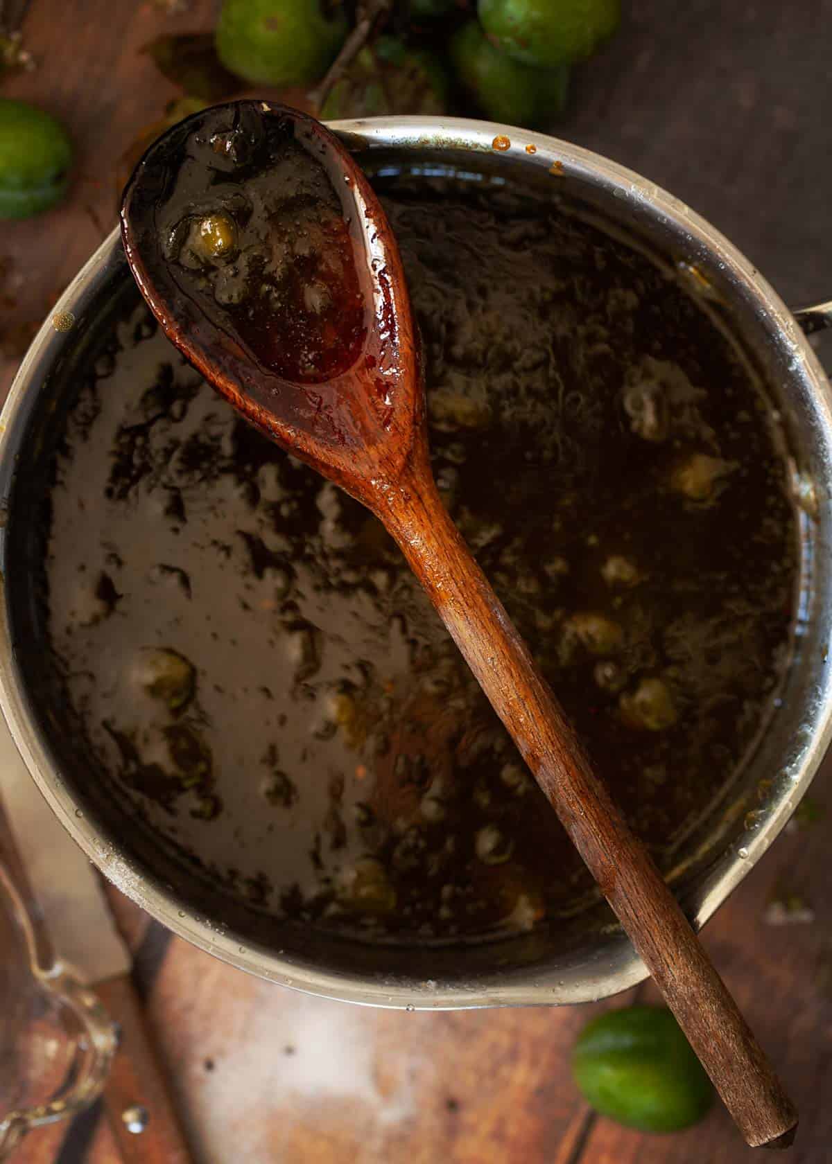 Process shot - cooked greengage jam in a saucepan with a wooden spoon resting on top