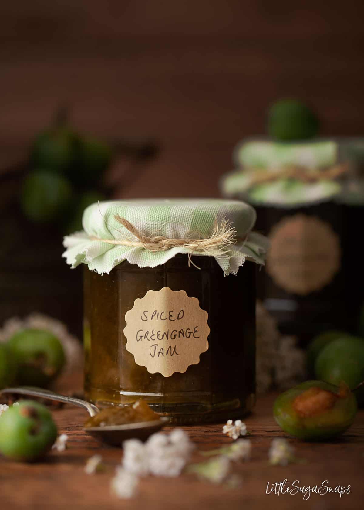 A jar of homemade greengage jam with fresh greengages on the tabletop.