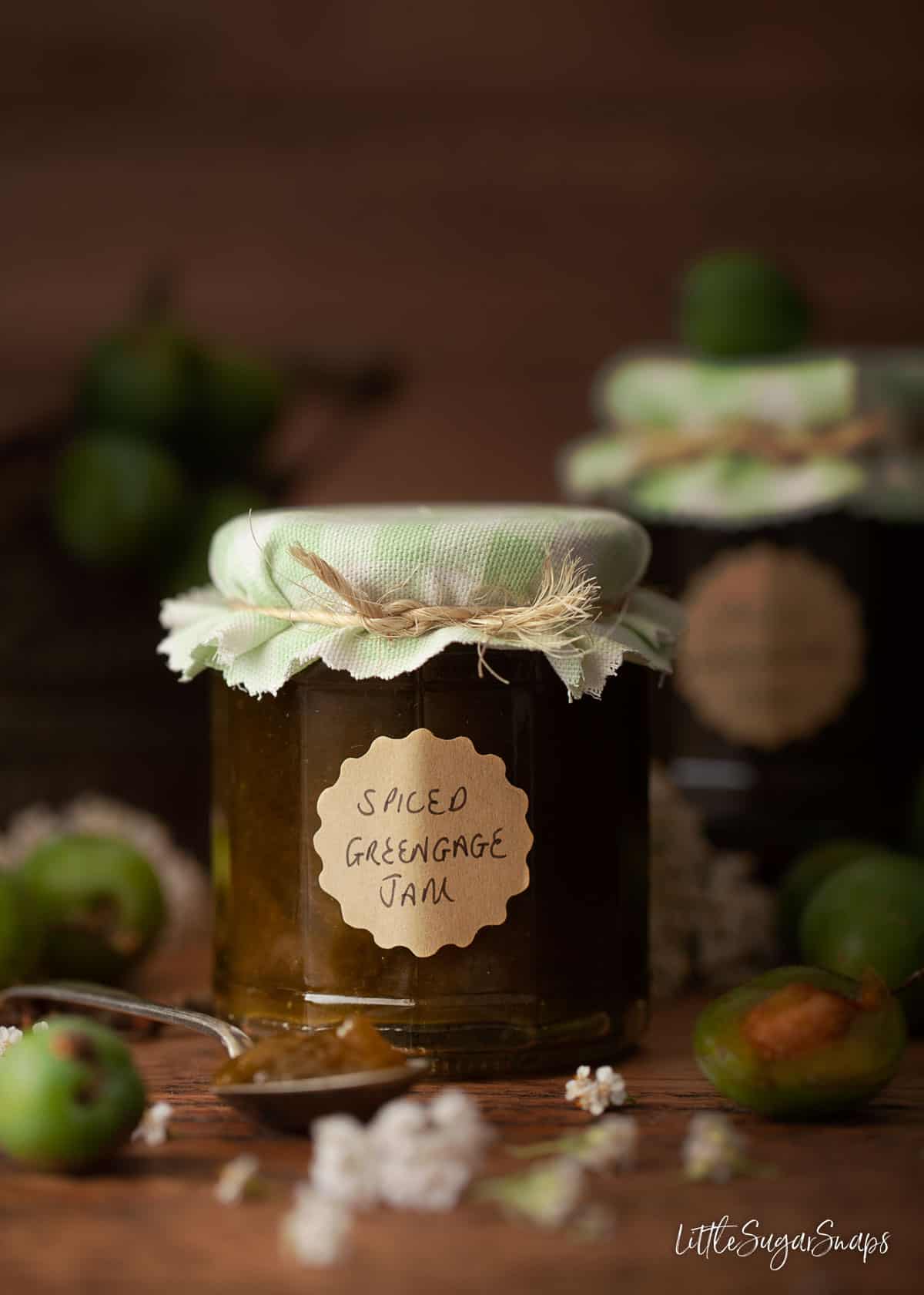 A jar of homemade greengage jam with fresh greengages on the tabletop. 