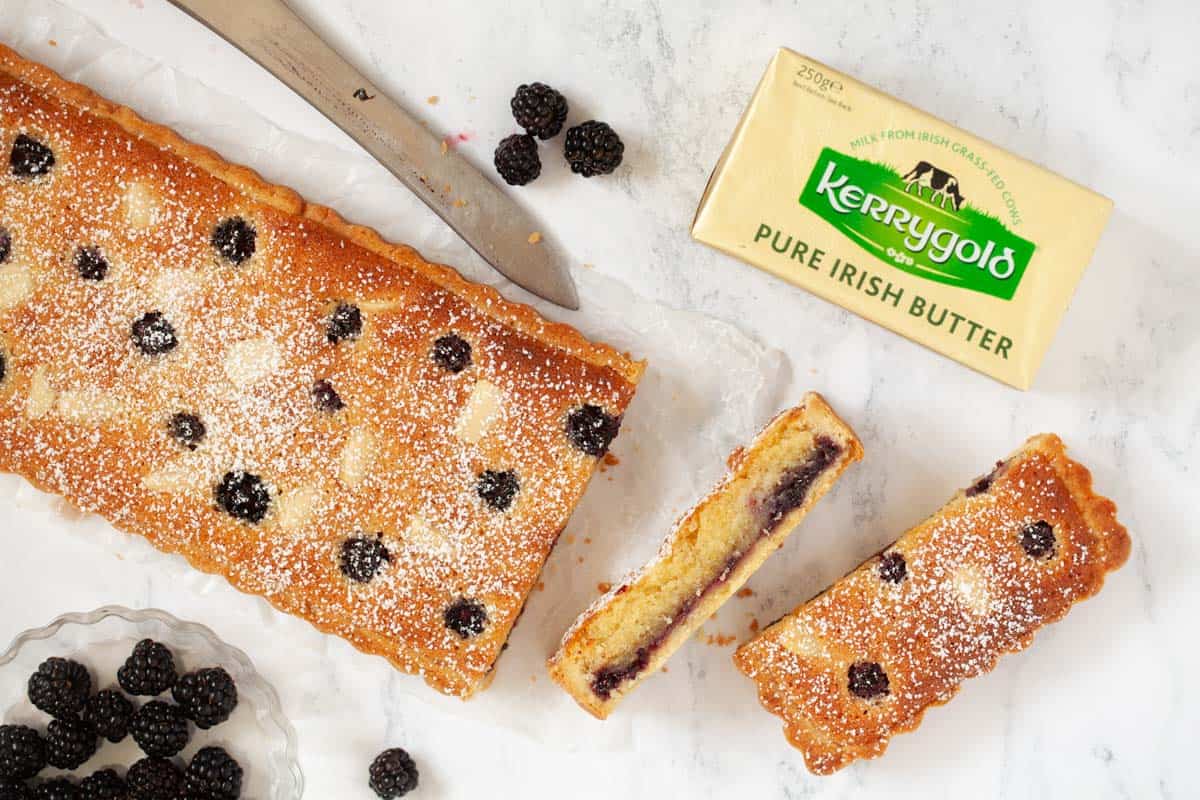 Slices cut from an oblong Almond frangipane tart with blackberries and butter