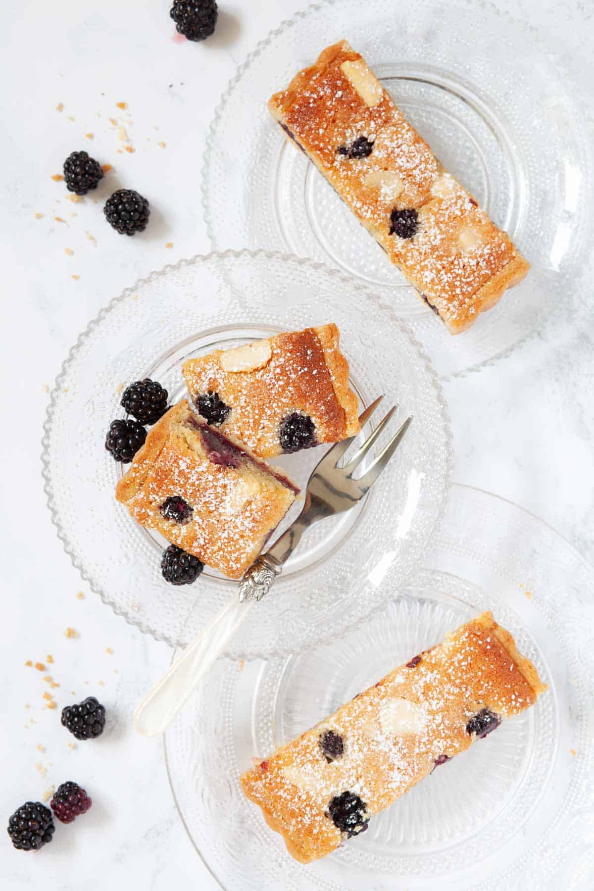 Slices of almond frangipane tart with blackberries on glass plates