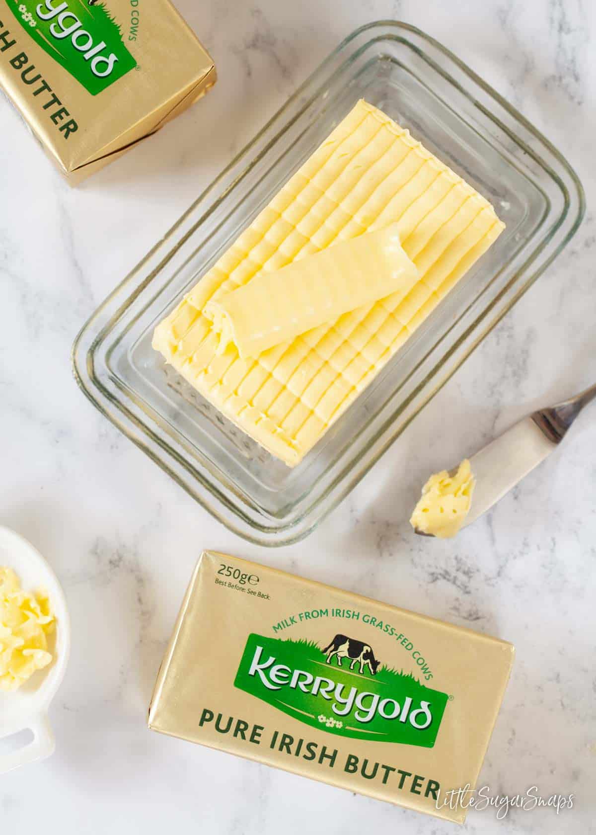 A slab of butter on a rectangular glass plate with unopened butter packs alongside
