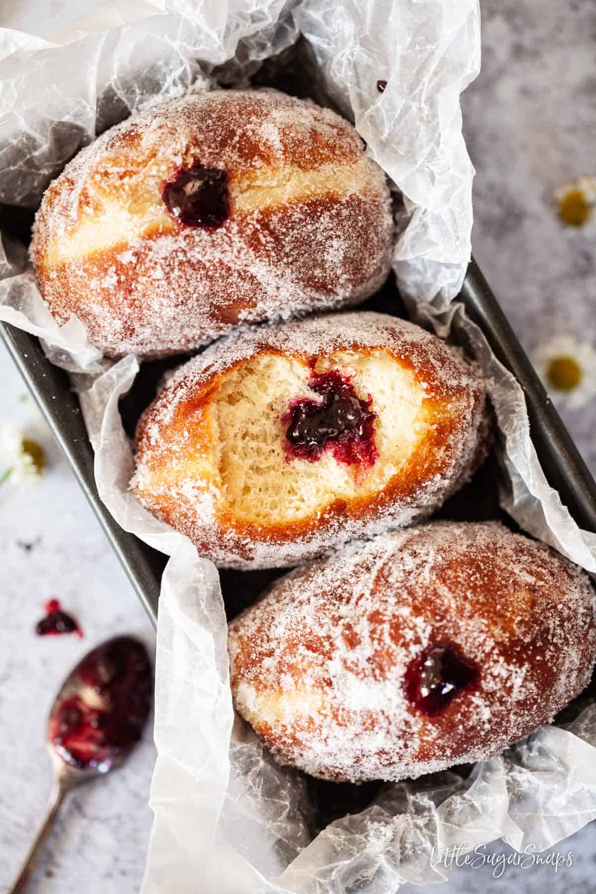 Three jam doughnuts in a loaf tin - one has been bitten into.