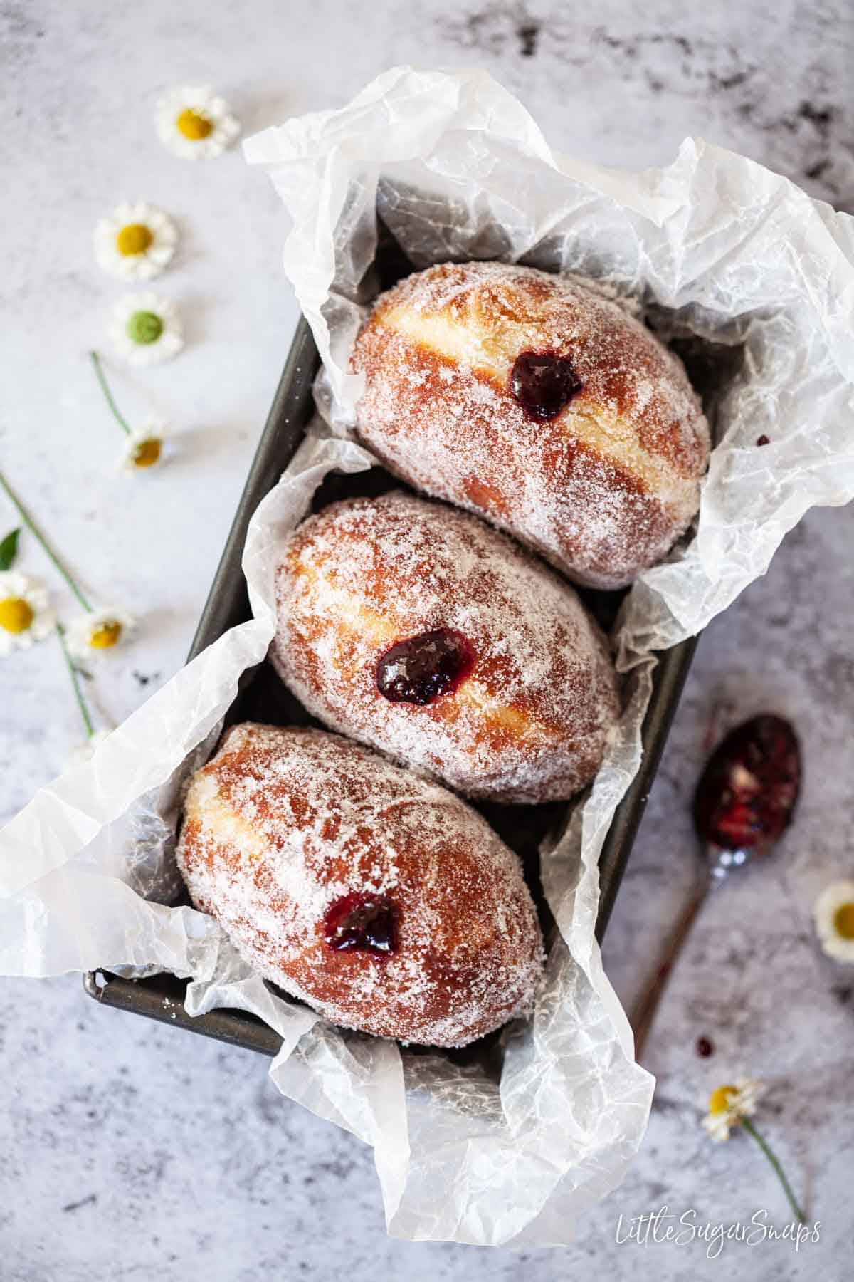 Three sugared doughnuts filled with jam in a baking tin