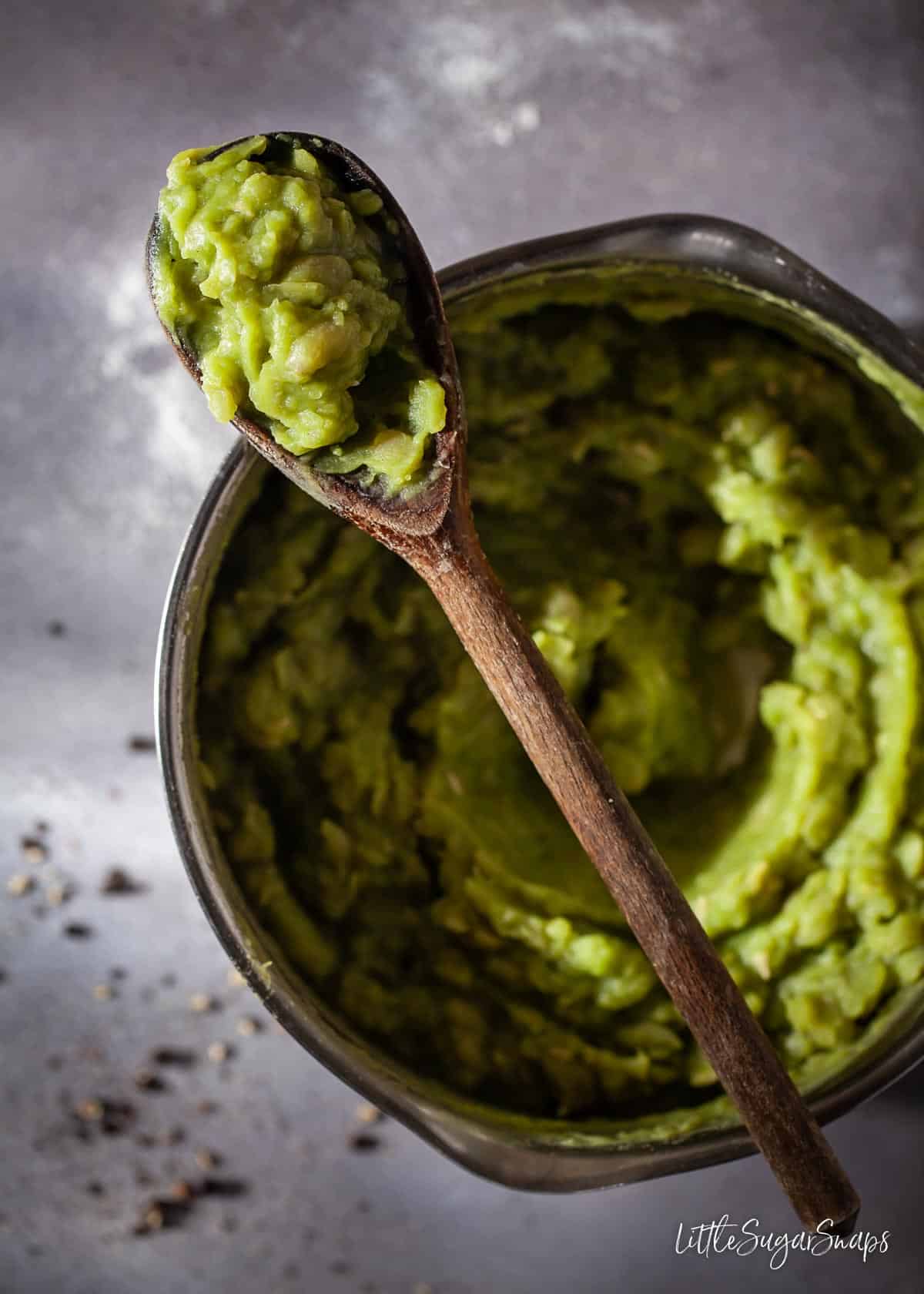 Homemade mushy peas in a saucepan with a wooden spoon resting on top.