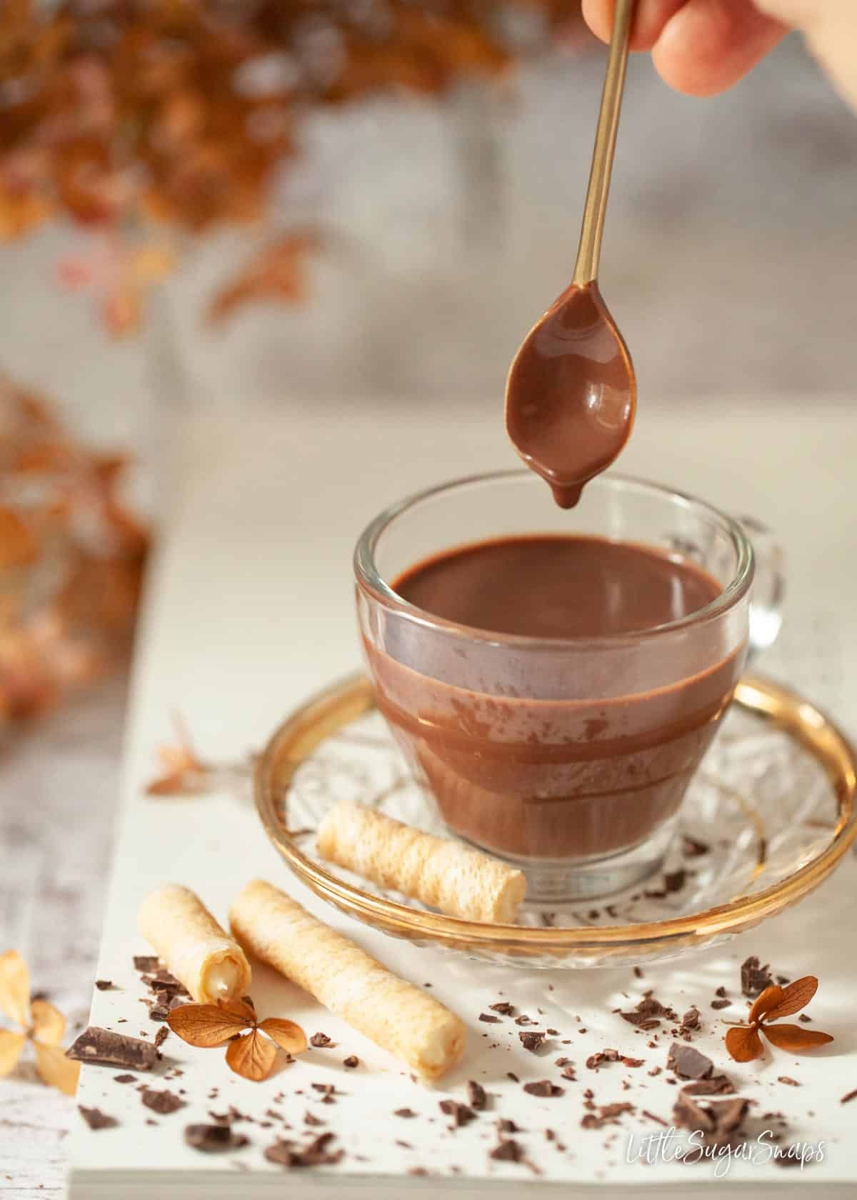 Thick Italian hot chocolate in a glass cup with a spoon being dipped in.