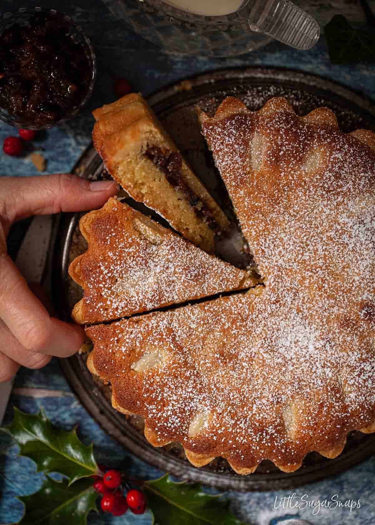 Person taking a slice of frangipane mince pie tart filled with mincemeat