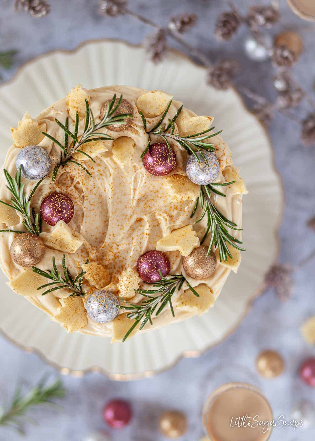 Overhead view of a festive cake decorated with mascarpone frosting, chocolates and rosemary