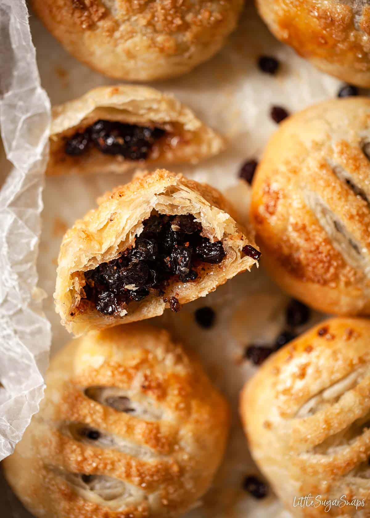 A cut open Eccles cake with whole ones on a tray