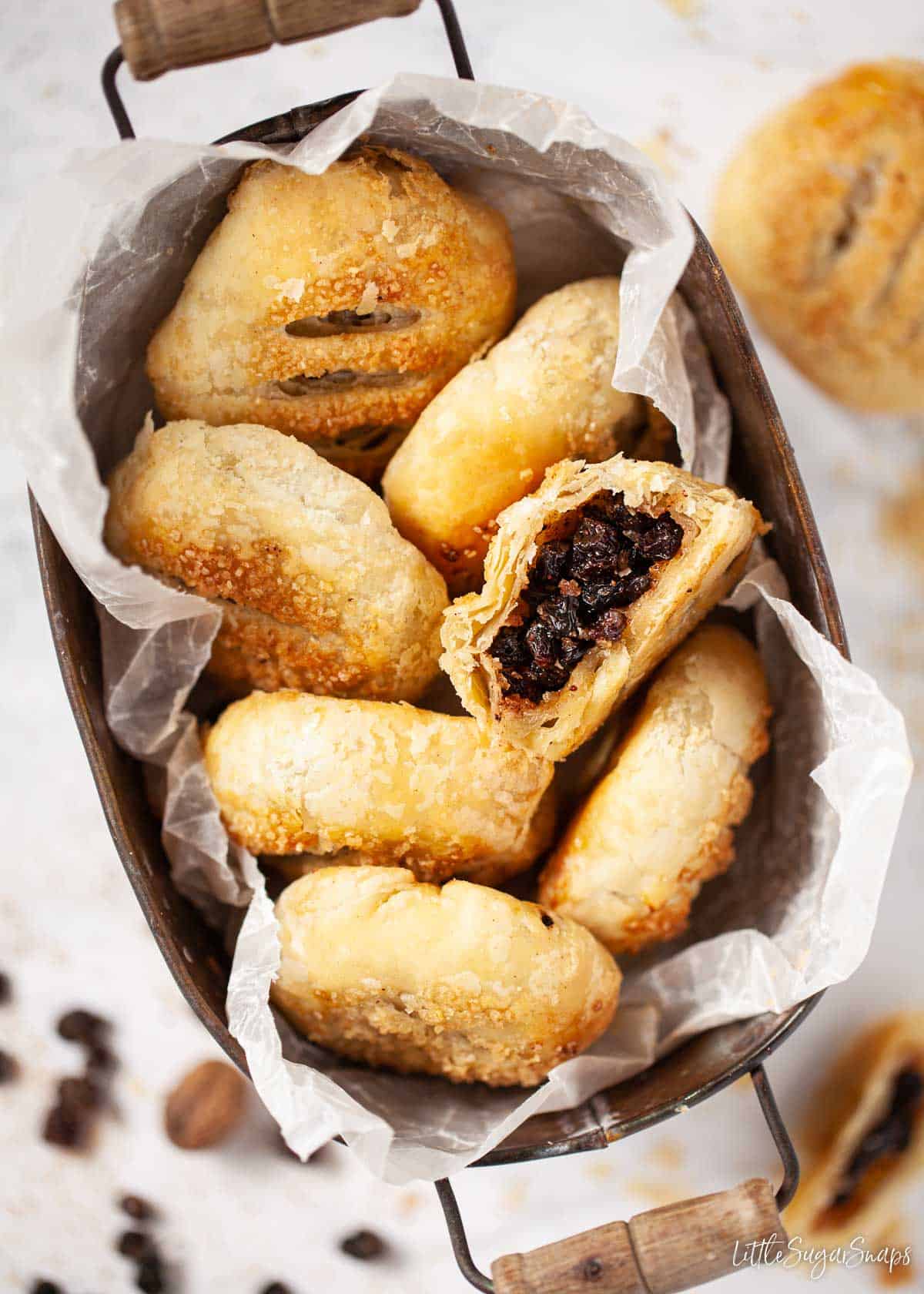 A tin of Eccles cakes with one cut open revealing the currant filling