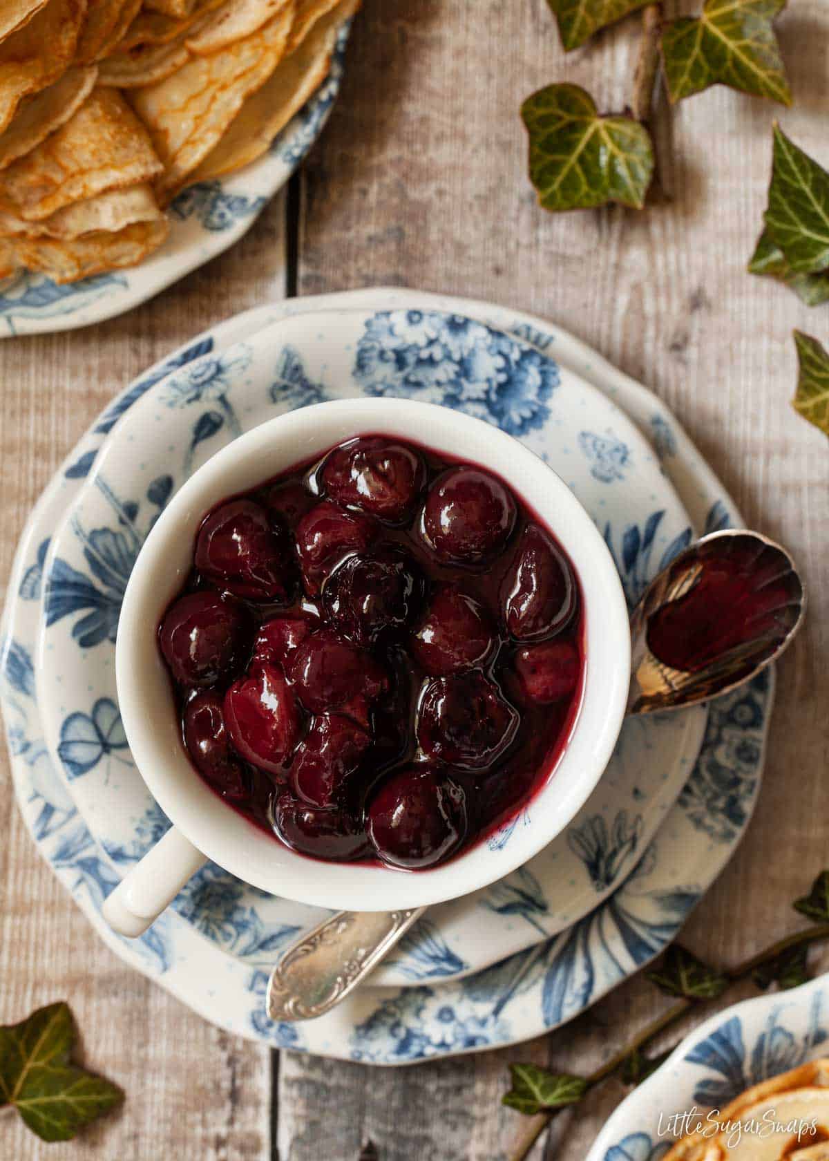 Cherries jubilee in a tea cup with pancakes on a plate next to it