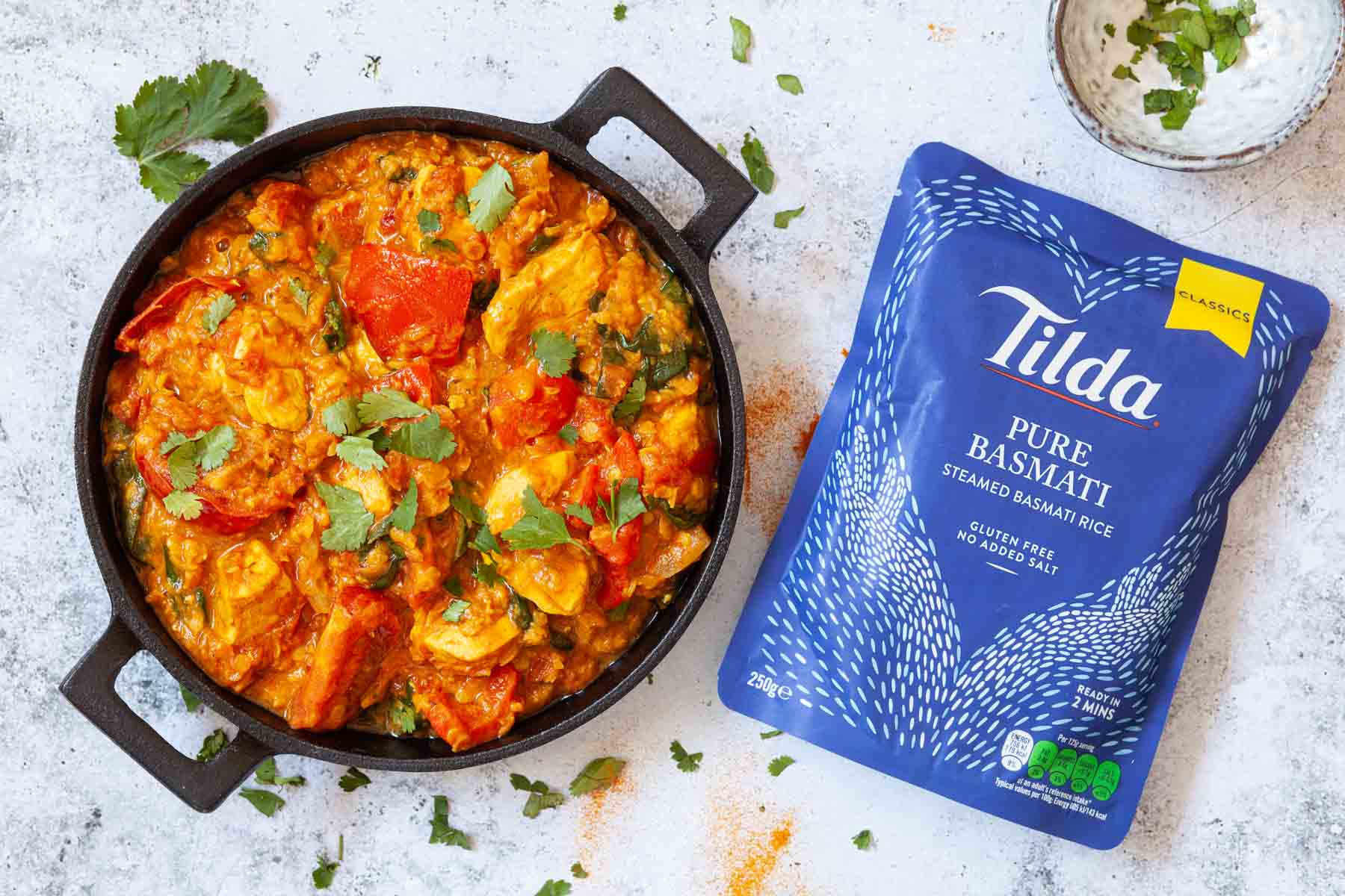 A skillet of chicken and lentil curry with a packet of microwaveable rice