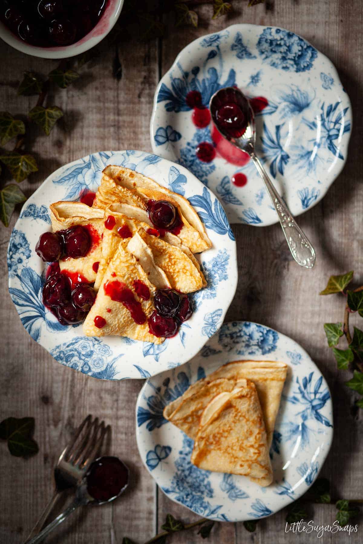 A plate of English thin pancakes with cherry sauce drizzled on top