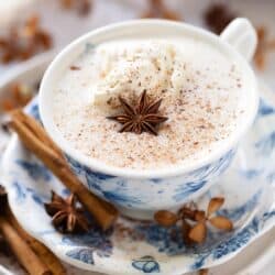 A cup of spiced hot chocolate with whipped cream, ground spice and star anise garnish