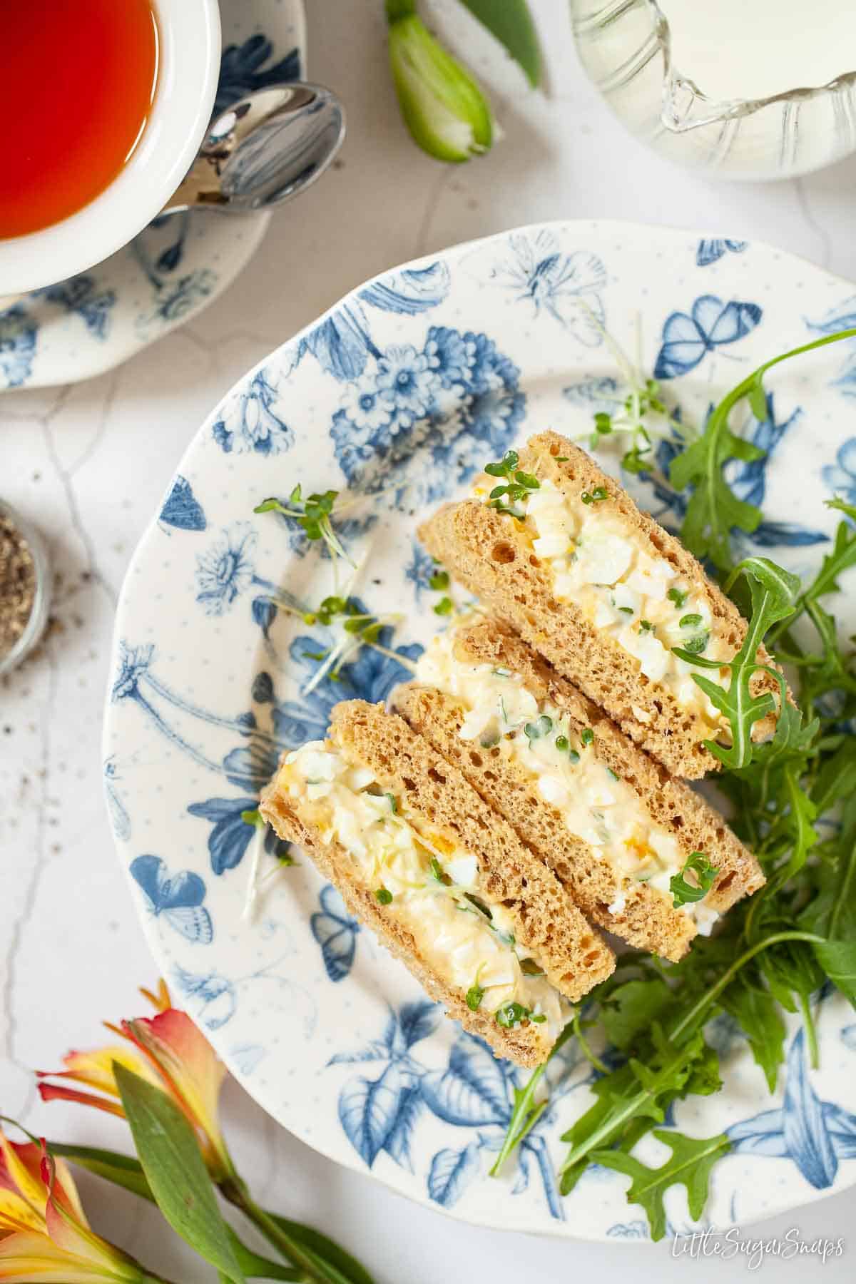 Three small rectangular egg mayo sandwiches on a floral plate