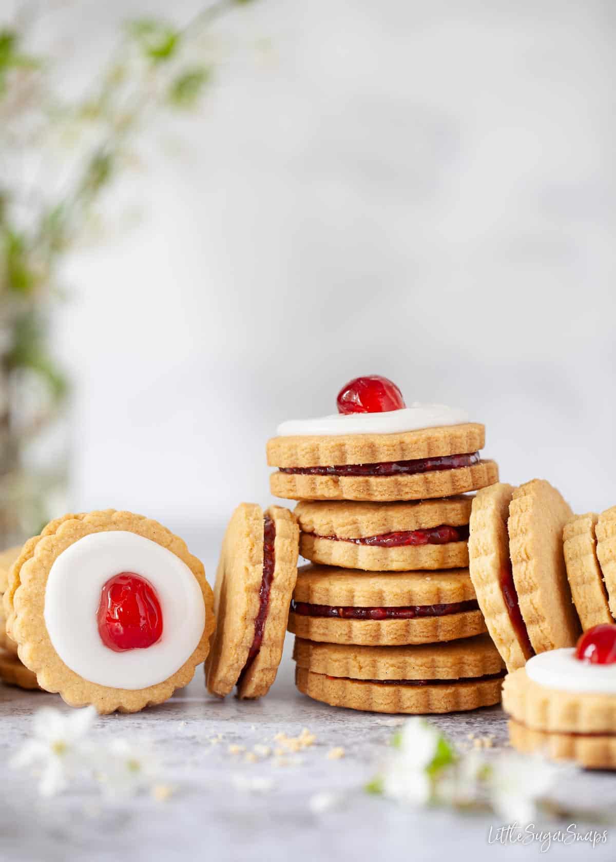 Empire biscuits stacked up. Some are iced and topped with cherries, some are not