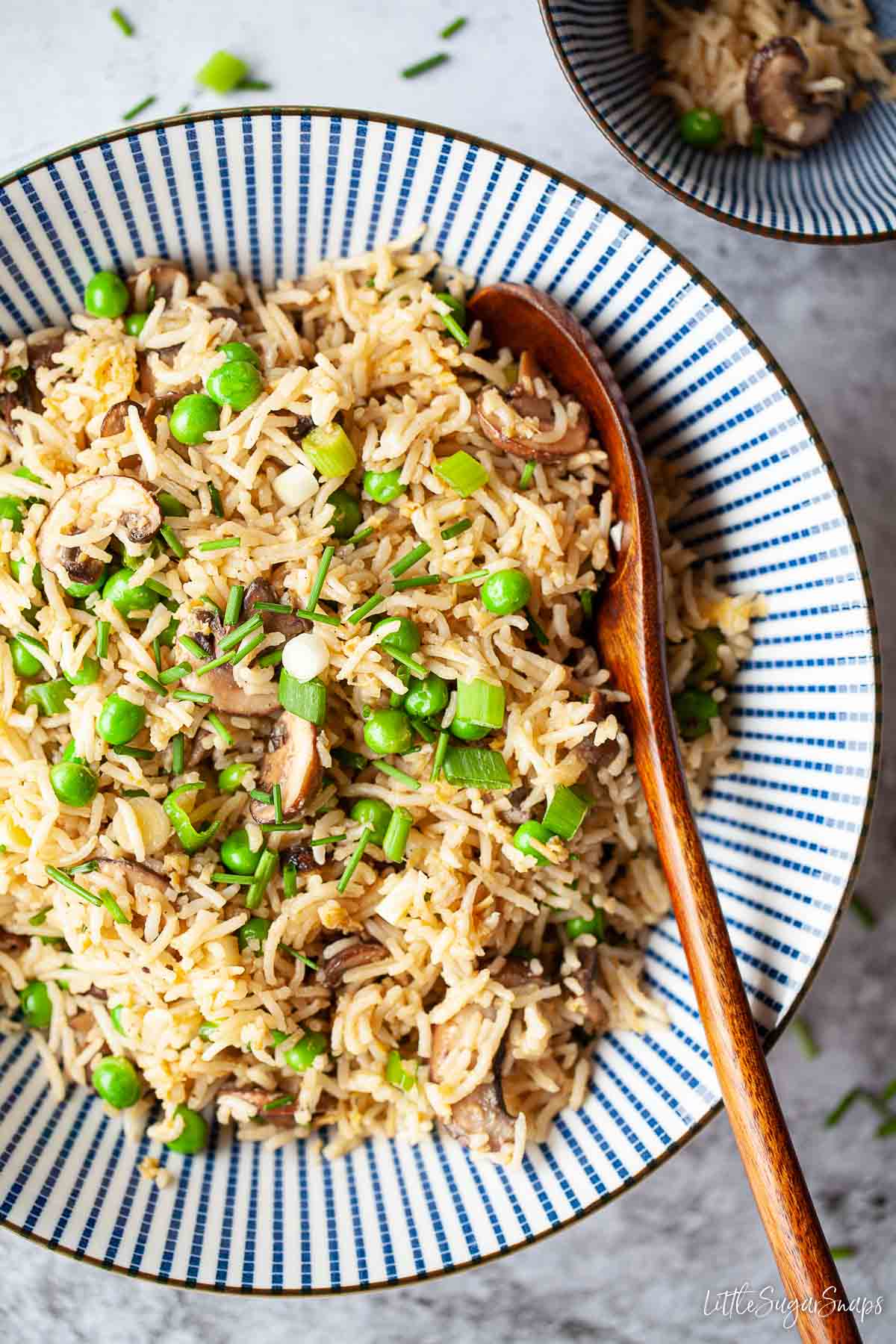 A bowl of fried rice with mushrooms with a serving spoon in it