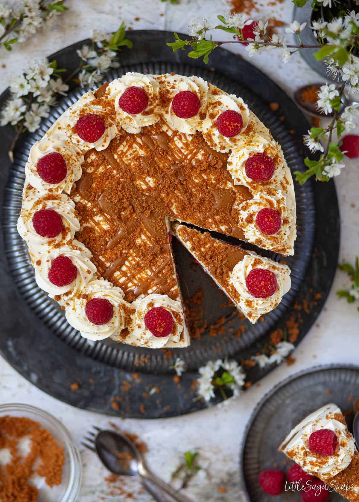 overhead view of no bake biscoff cheesecake with raspberries. It's partially cut into slices