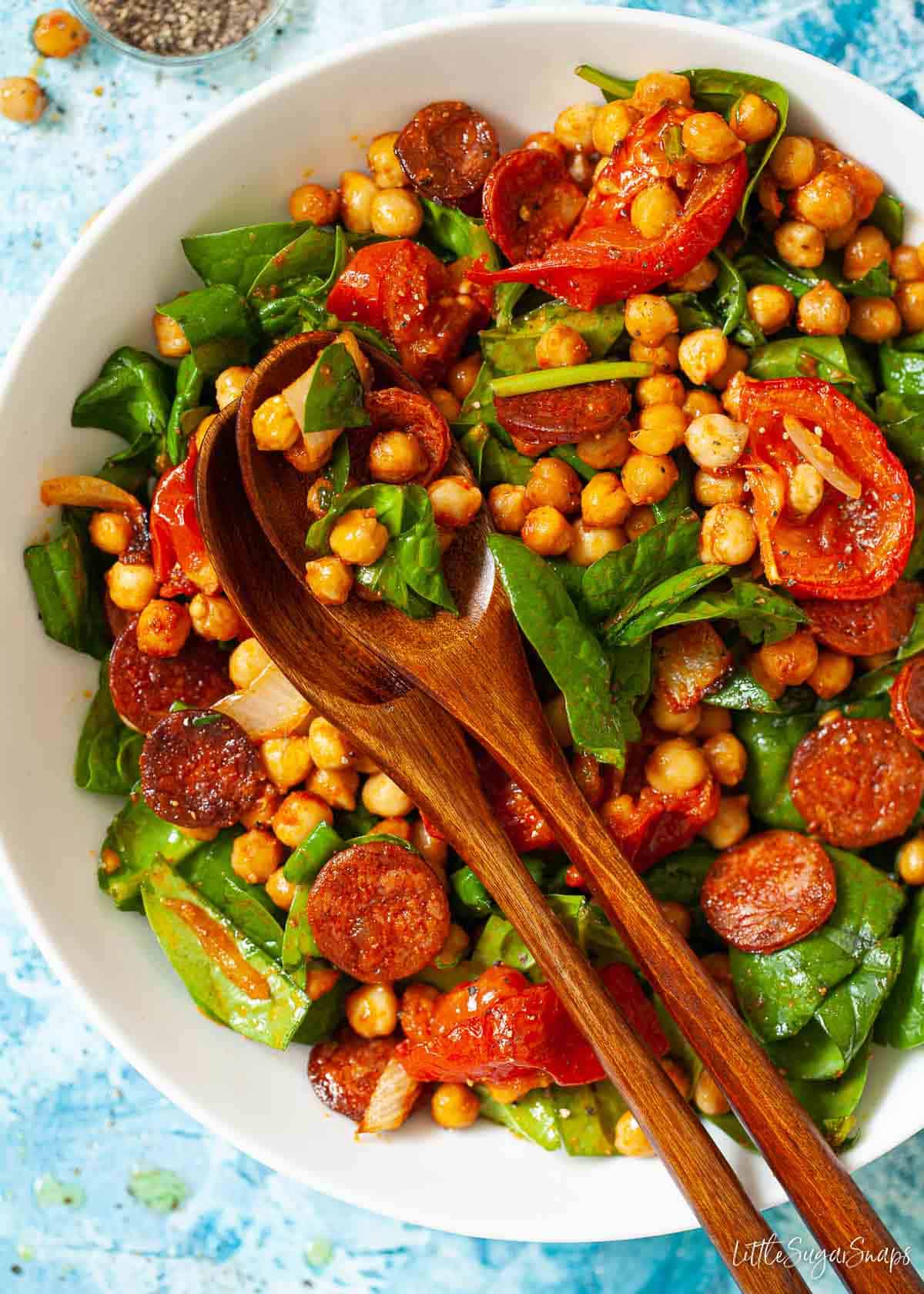 Dressed salad in a bowl with wooden serving spoons resting on top