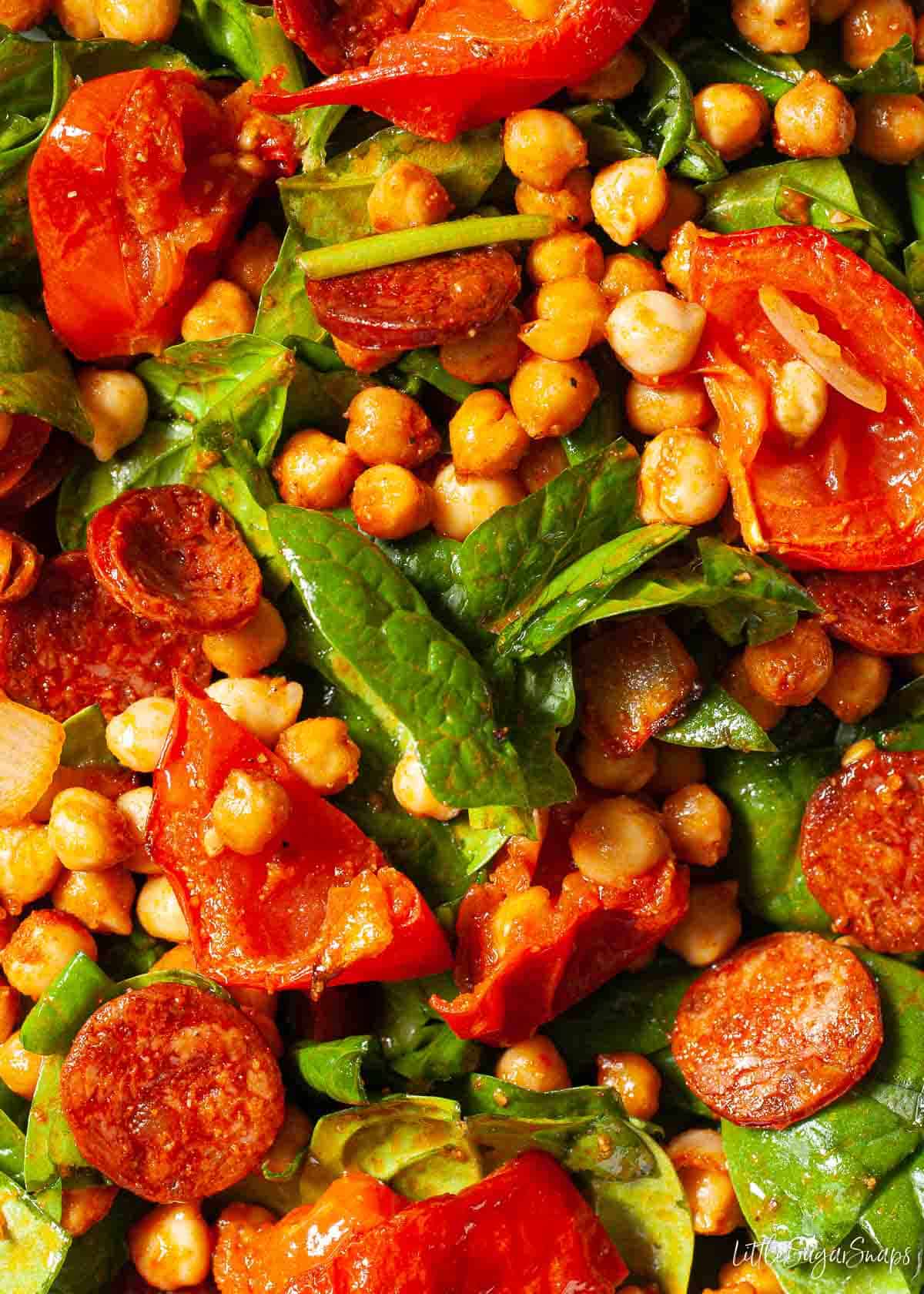 Close up view of roasted chickpea salad with spinach, tomatoes and chorizo