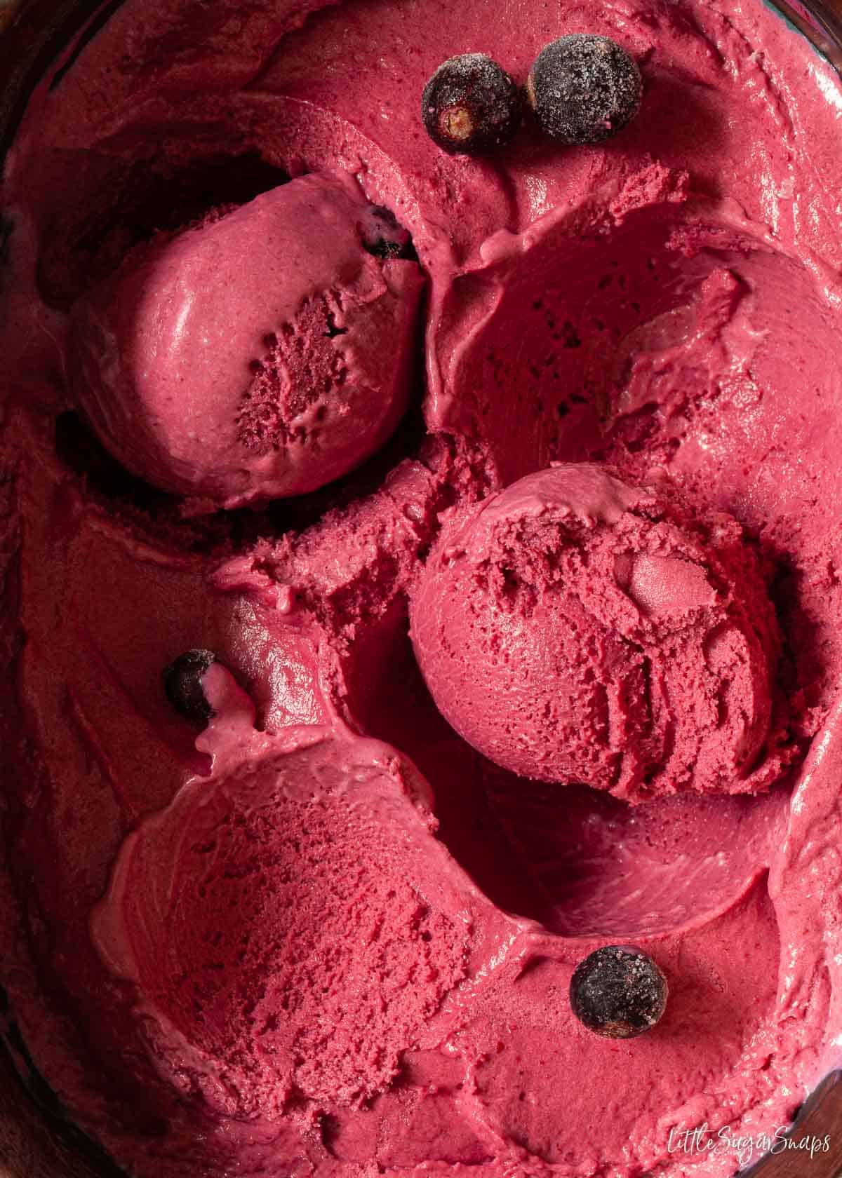 Close up of a tub of homemade blackcurrant ice cream with some scooped into balls