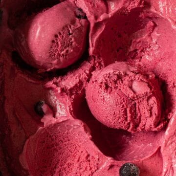 Close up of a tub of homemade blackcurrant ice cream with some scooped into balls