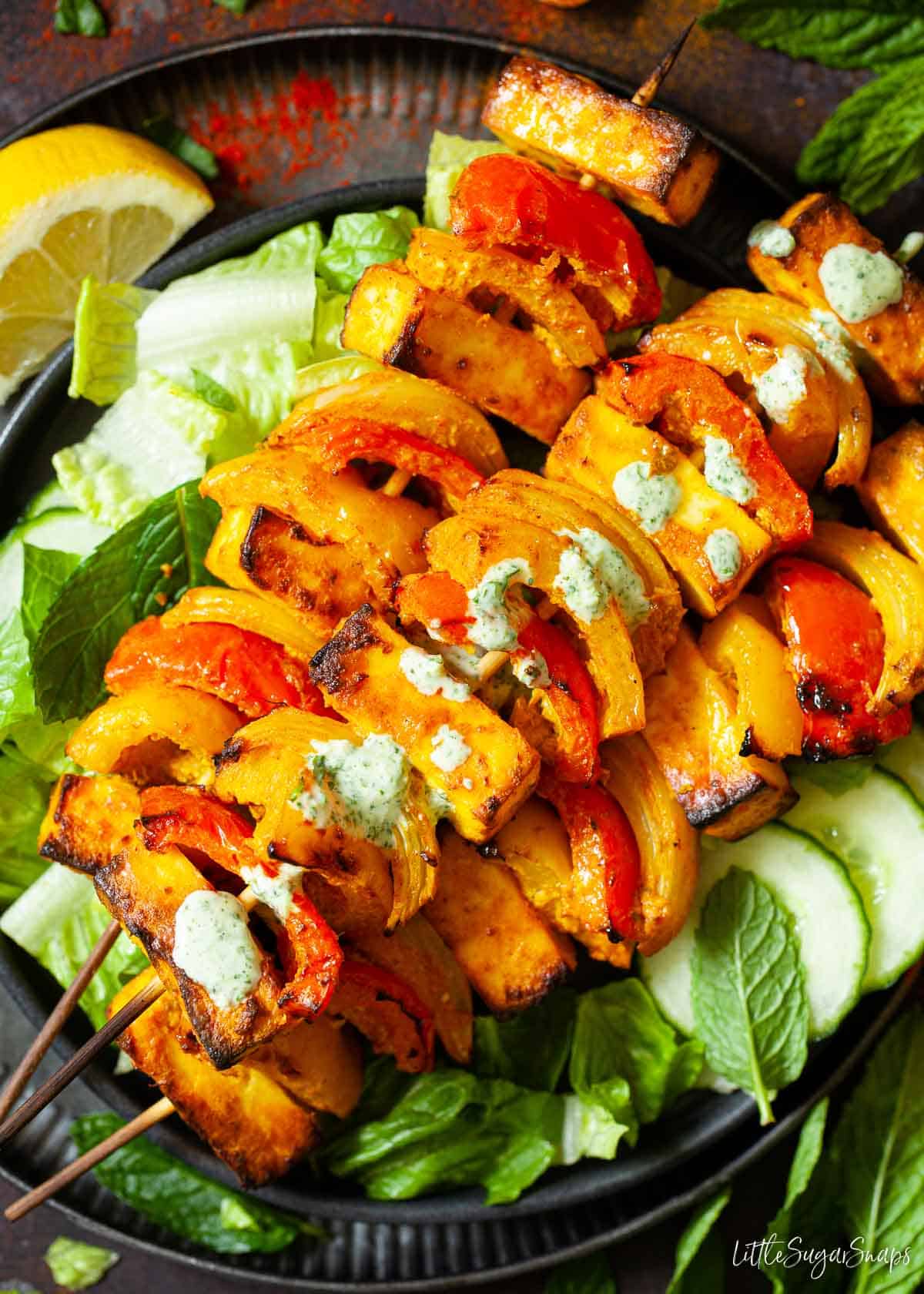 Paneer tikka kebabs on green salad with yoghurt sauce drizzled on top