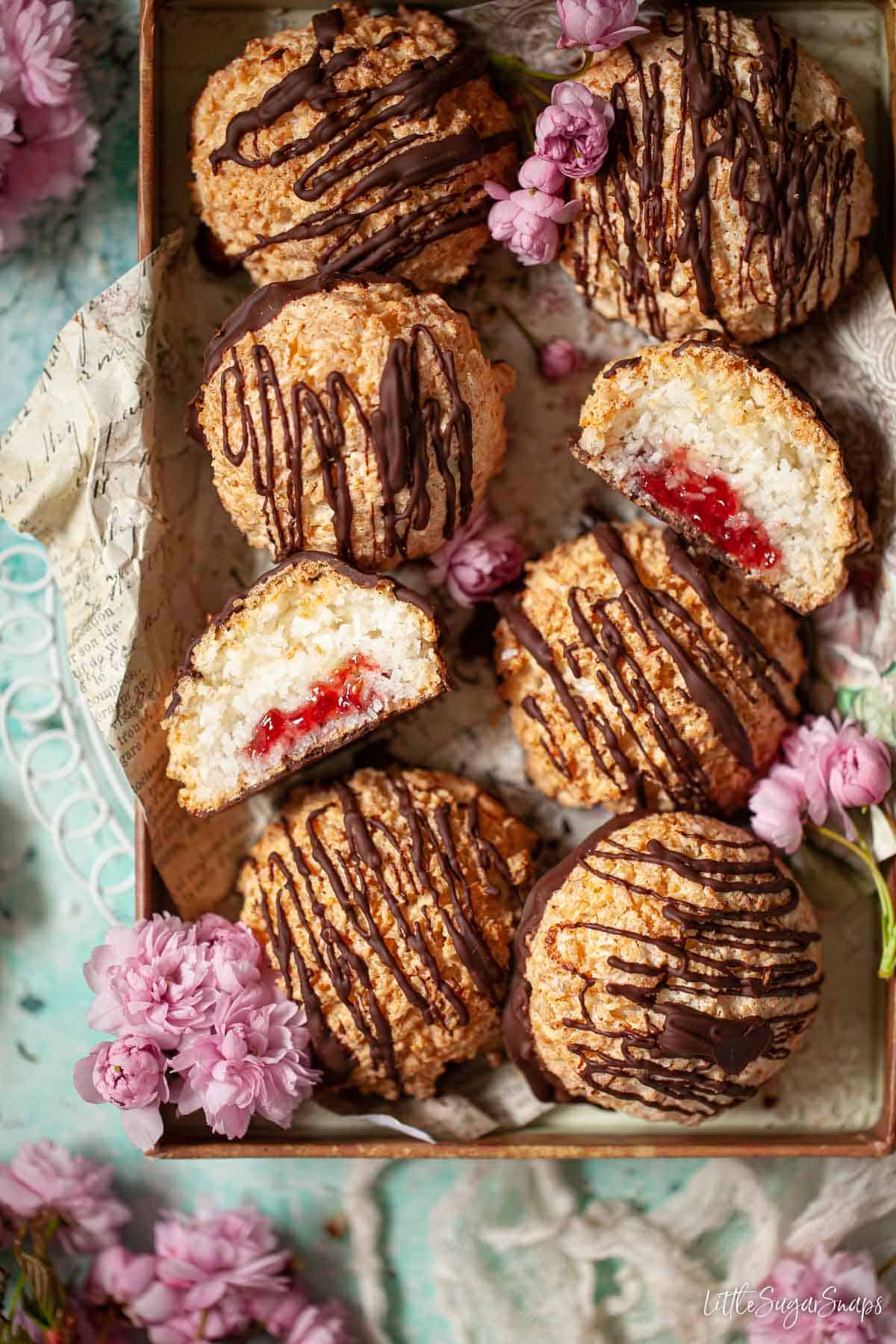 A tray of jam-filled rochers coco topped with chocolate drizzle. One is cut open