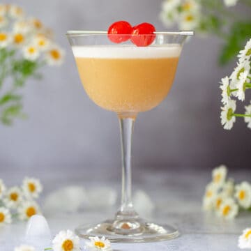 An Amaretto sour cocktail garnished with egg white foam and cocktail cherries