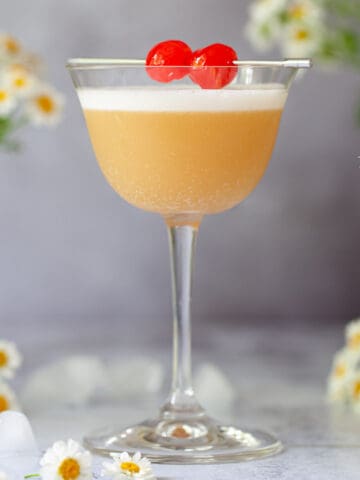 An Amaretto sour cocktail garnished with egg white foam and cocktail cherries