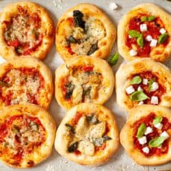 n assortment of pizzette - mini pizzas - on a baking sheet including meat pizza, vegetarian pizza and vegan pizza