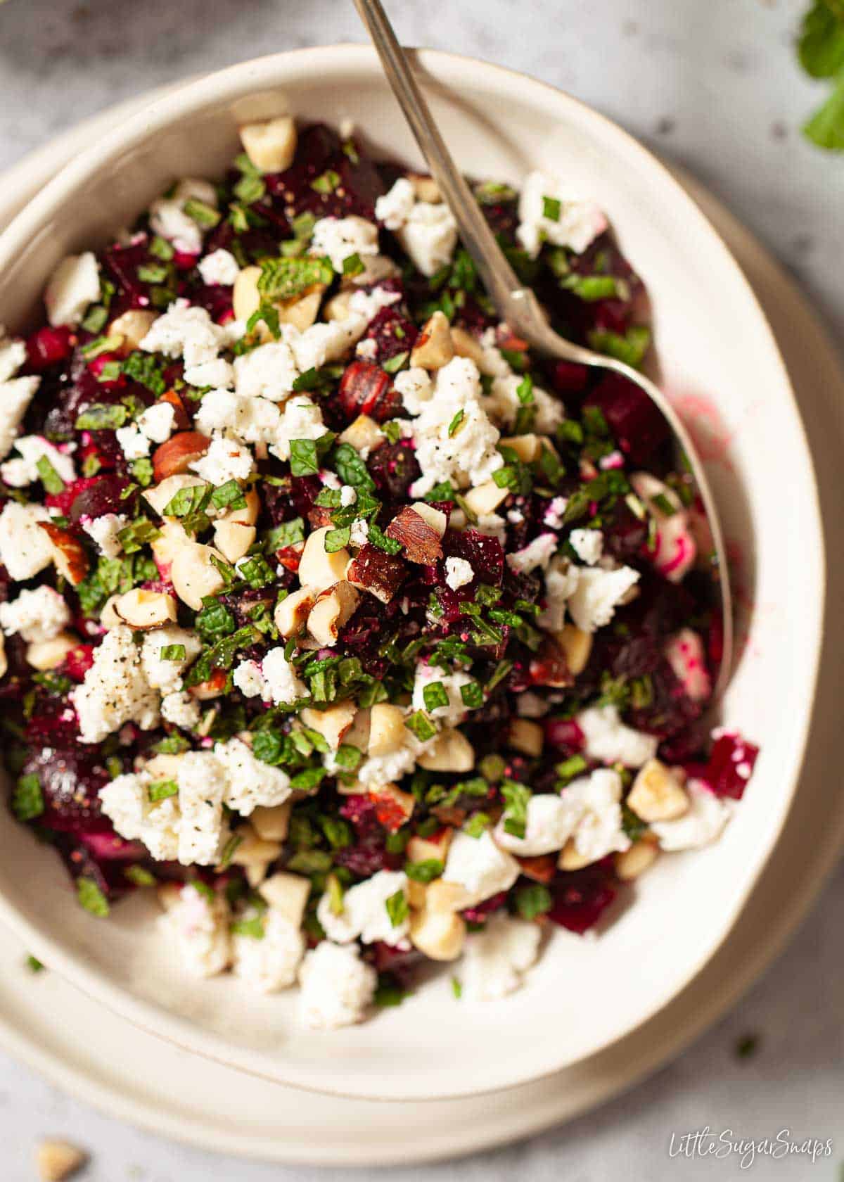 A bowl of mixed beetroot salad featuring cubed beets, crumbled feta, chopped mint and chopped nuts.