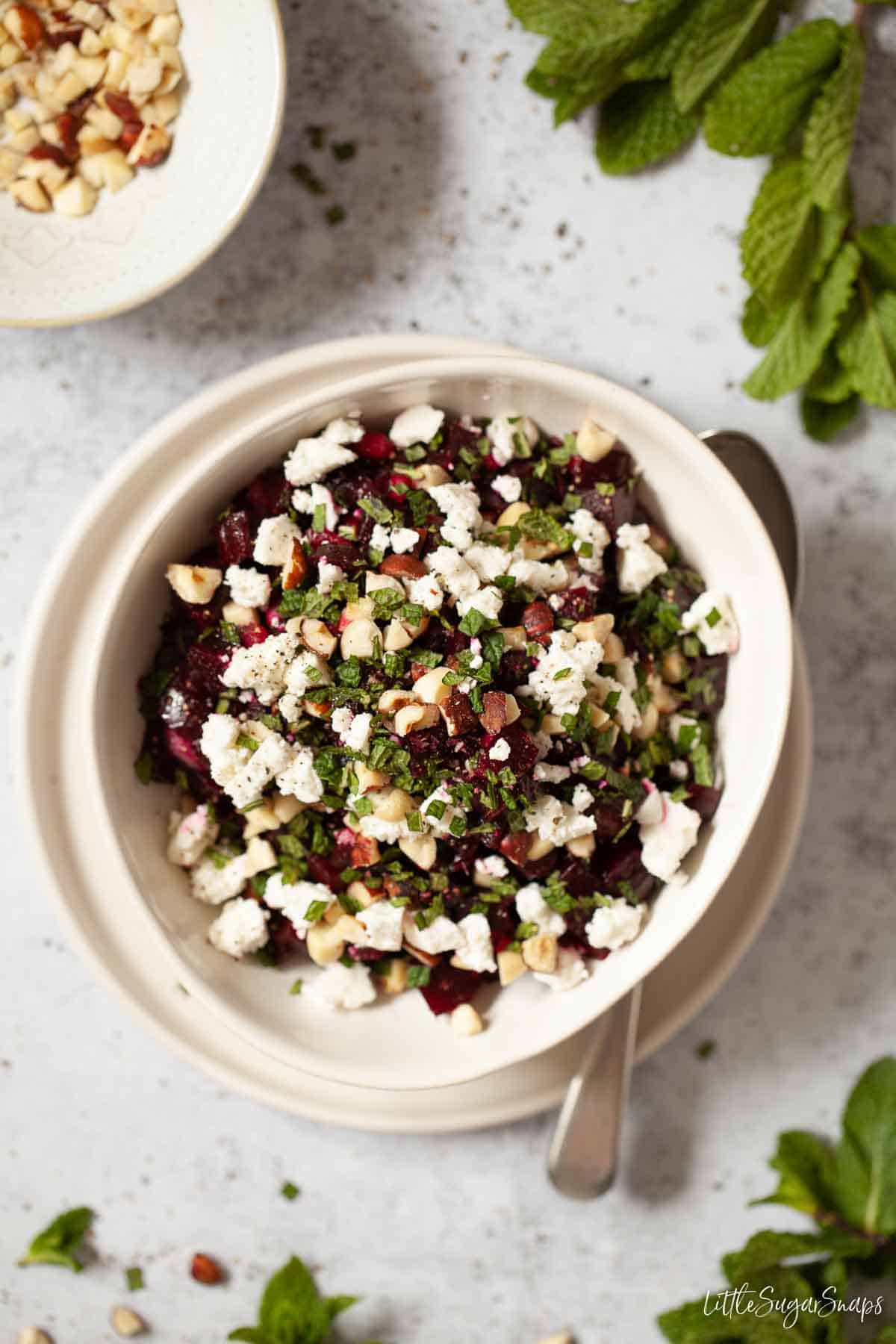 A bowl of beetroot and feta cheese in a bowl with a serving spoon alongside