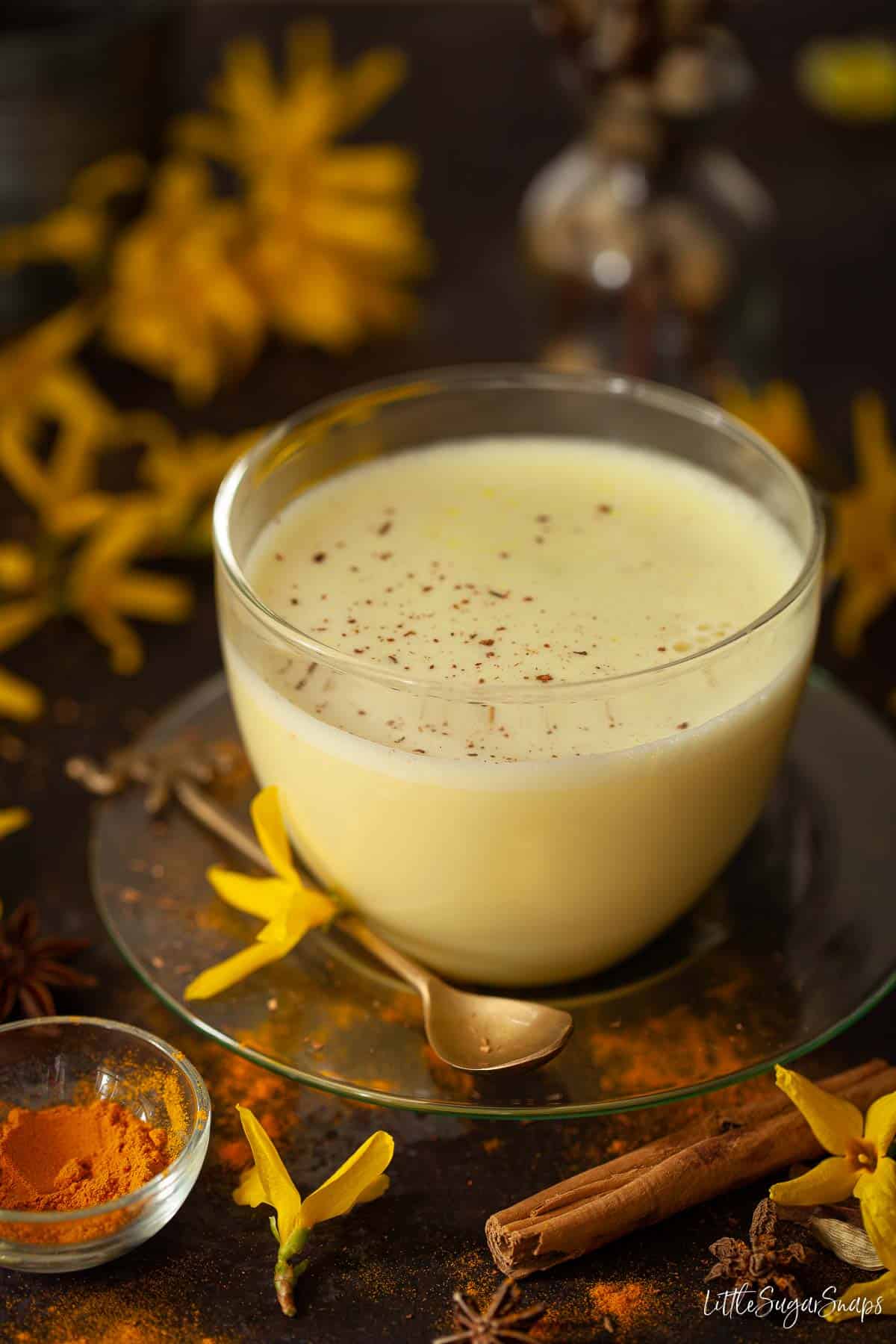 A golden milk latte in a clear glass mug dusted with ground spices