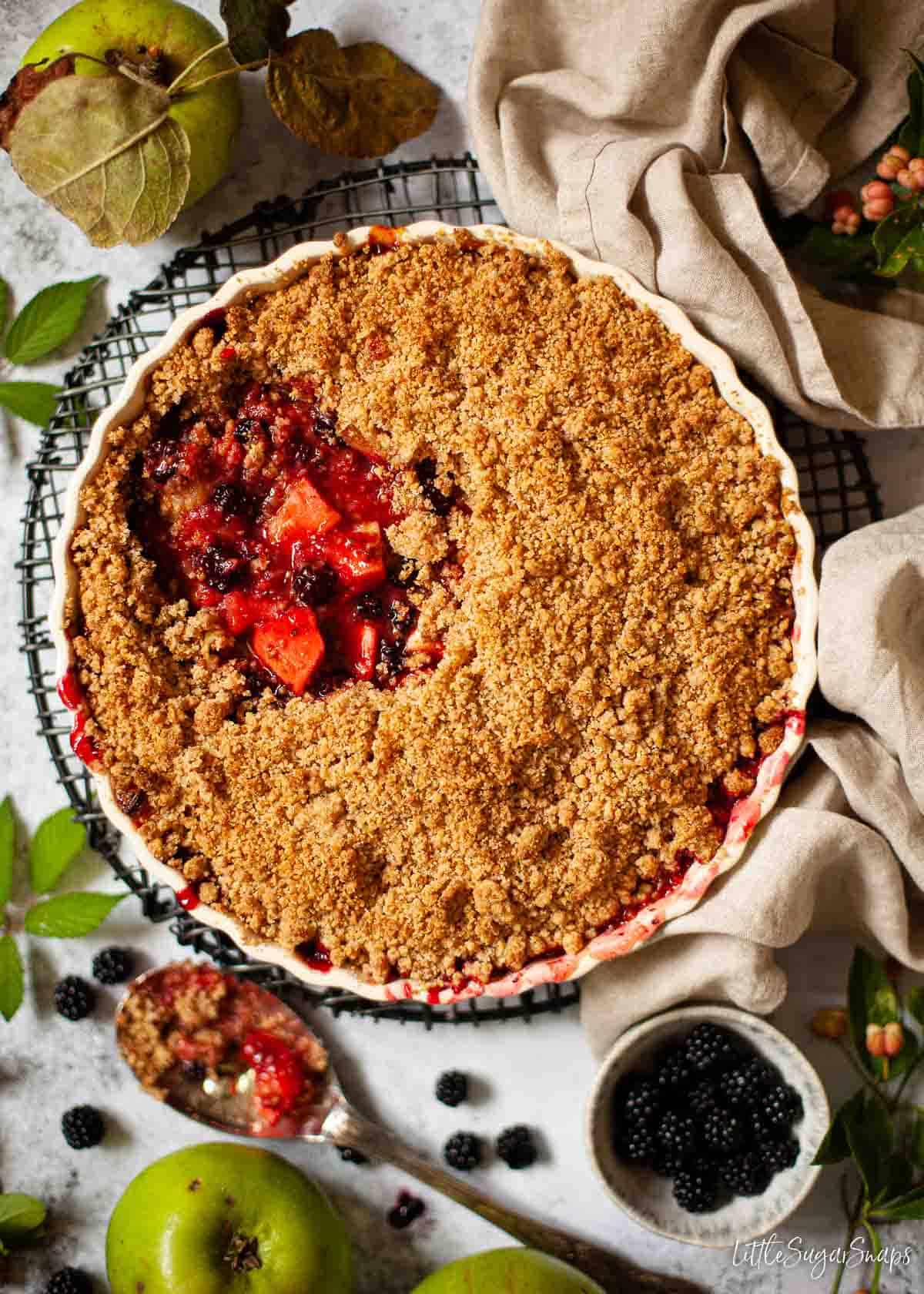 A bowl of apple and blackberry crumble with a portion removed